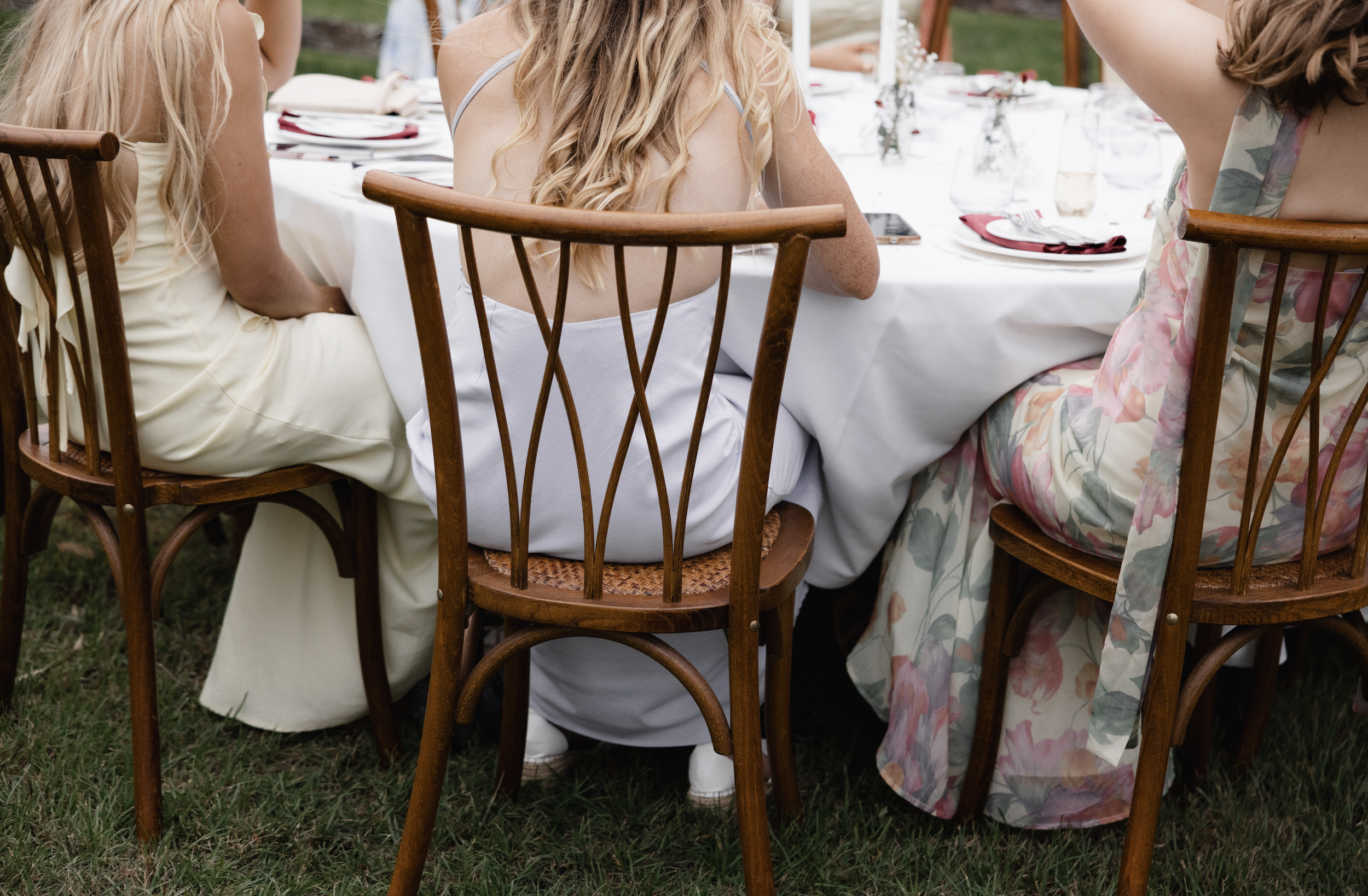 Three women sitting at a table outdoors during a social gathering, with plates and glasses on the table.
