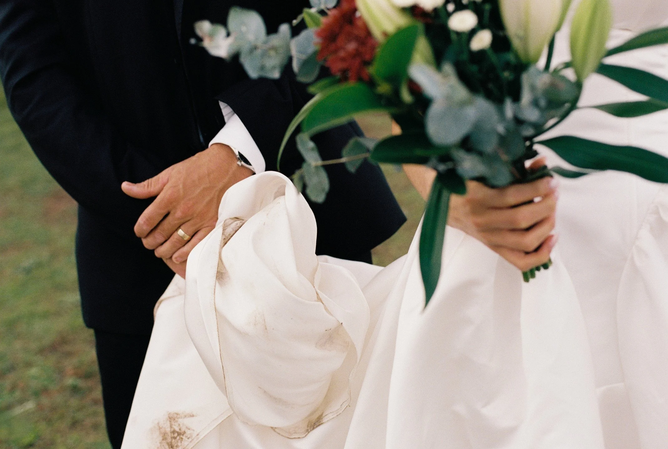 A person holding a bouquet of flowers, wearing a black suit with a white shirt and a ring on their left hand.