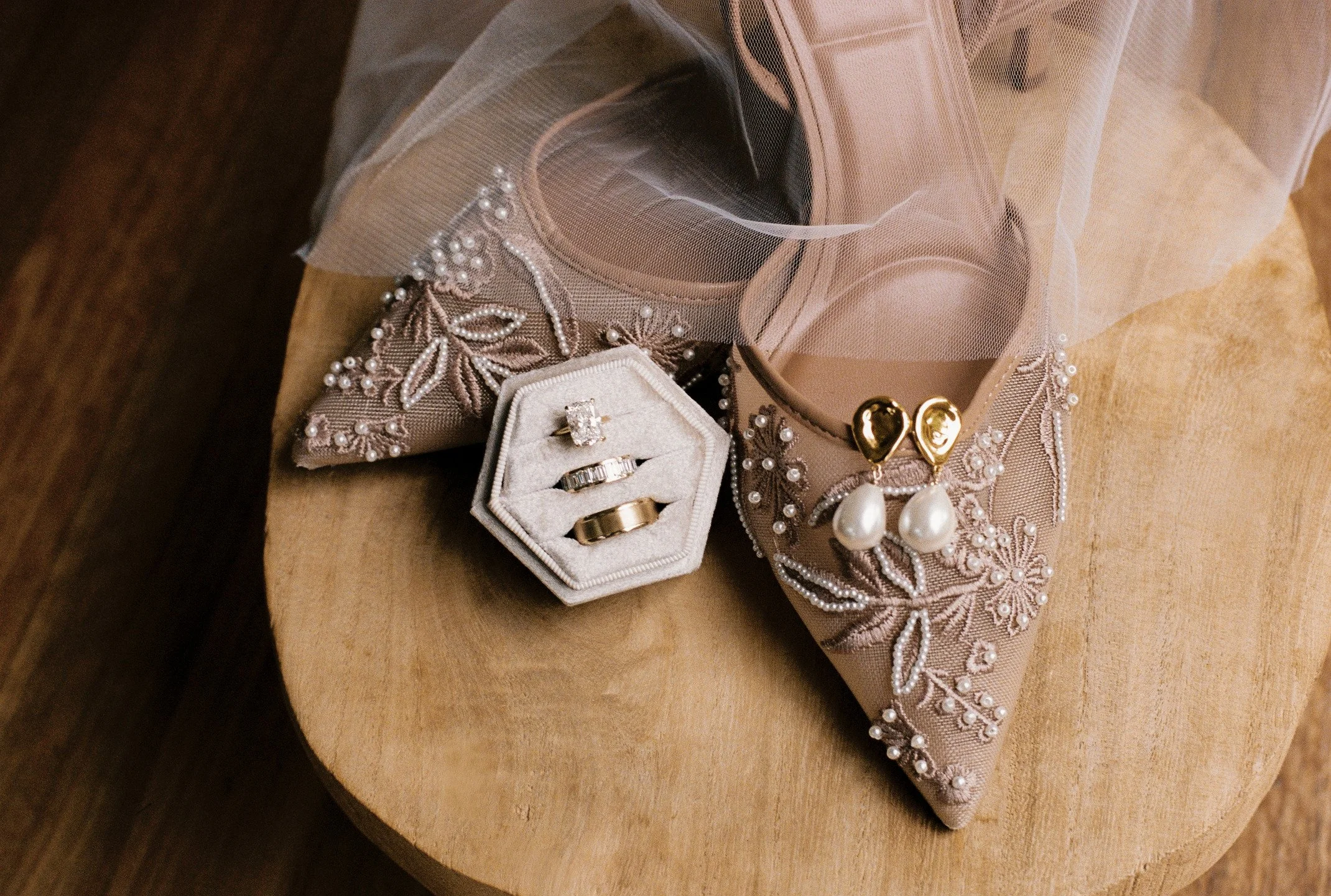 Jewelry and accessories, including rings, earrings, and a necklace, displayed in a small open box and on decorative fabric with pearl and floral embroidery.