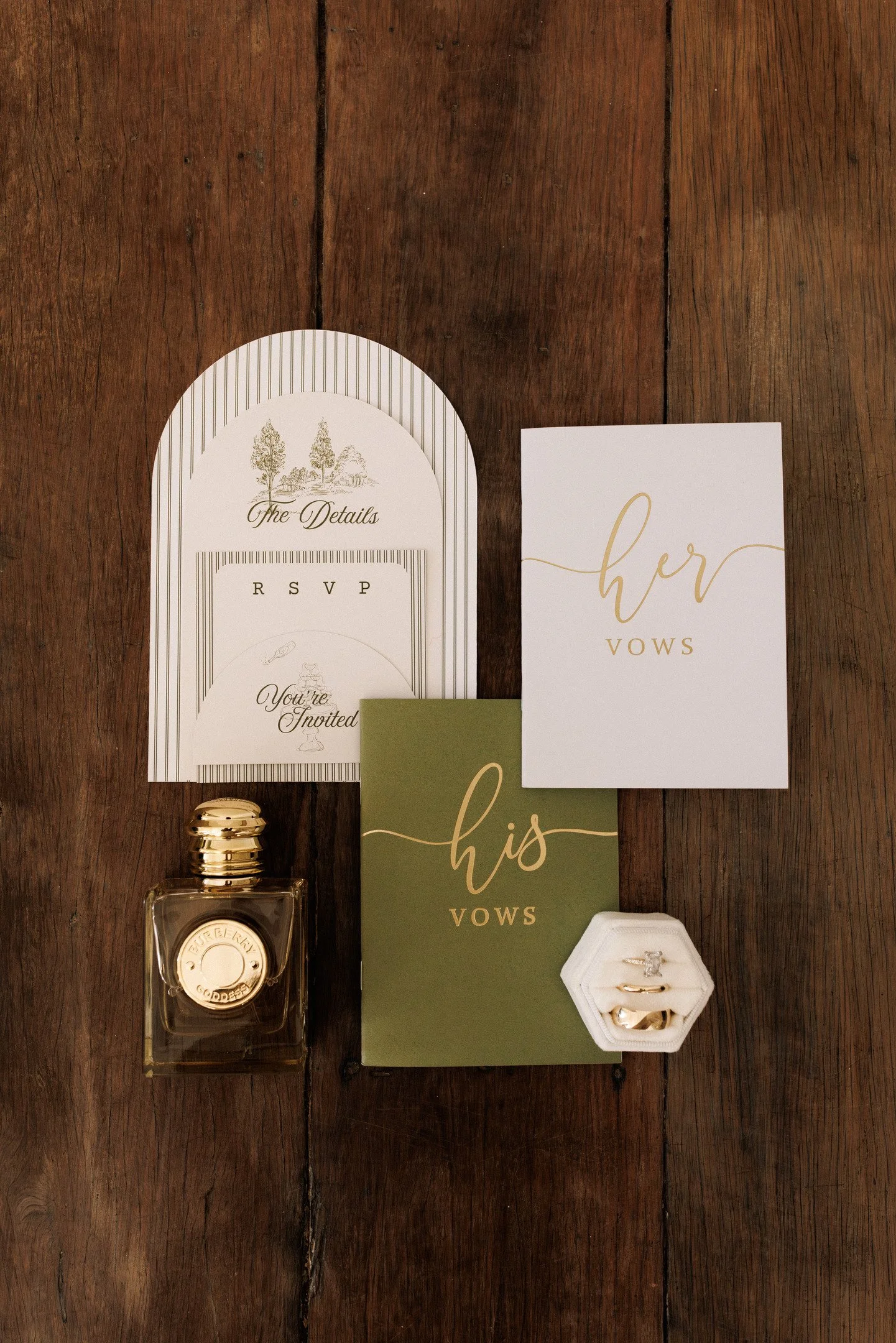 Wedding invitation suite including RSVP and vow cards, and a small jewelry box with rings, on a wooden table.