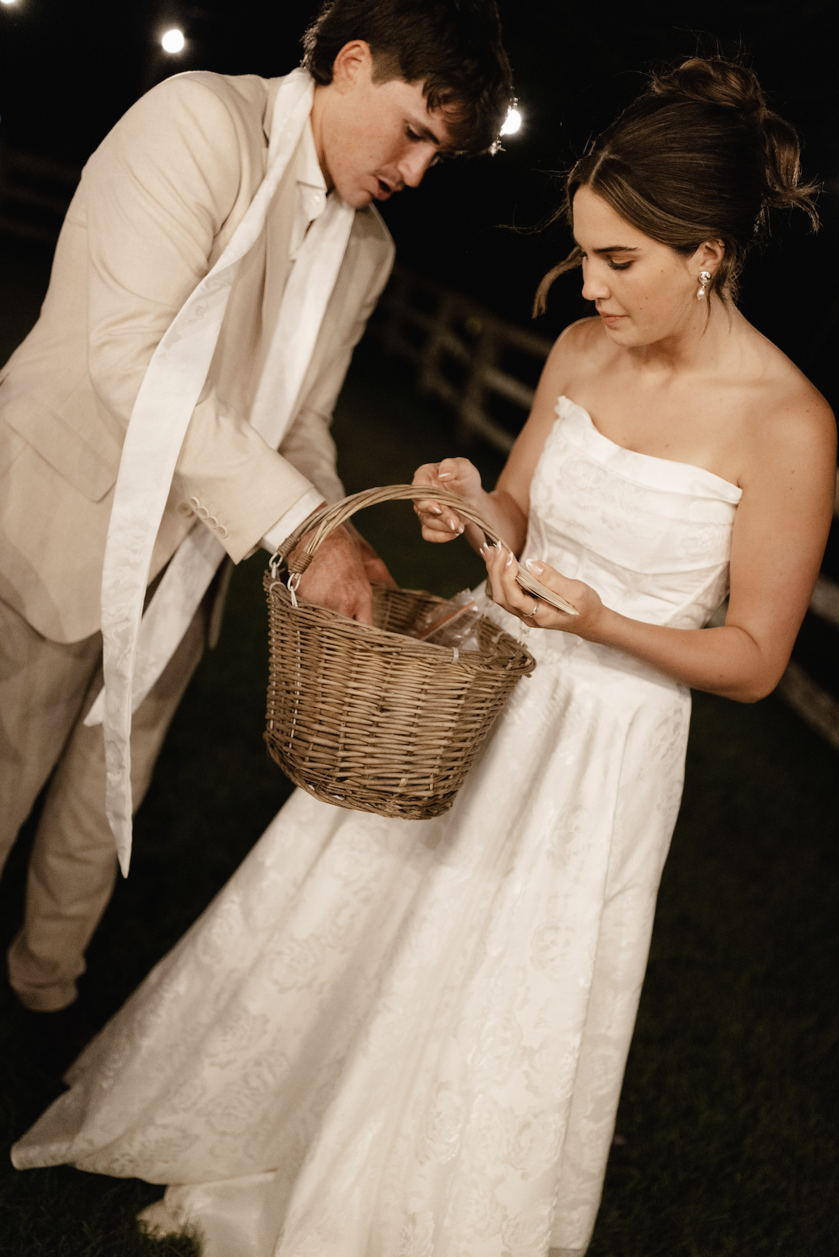 Bride and groom at their wedding, the groom is grabbing something from a basket that the bride is holding.