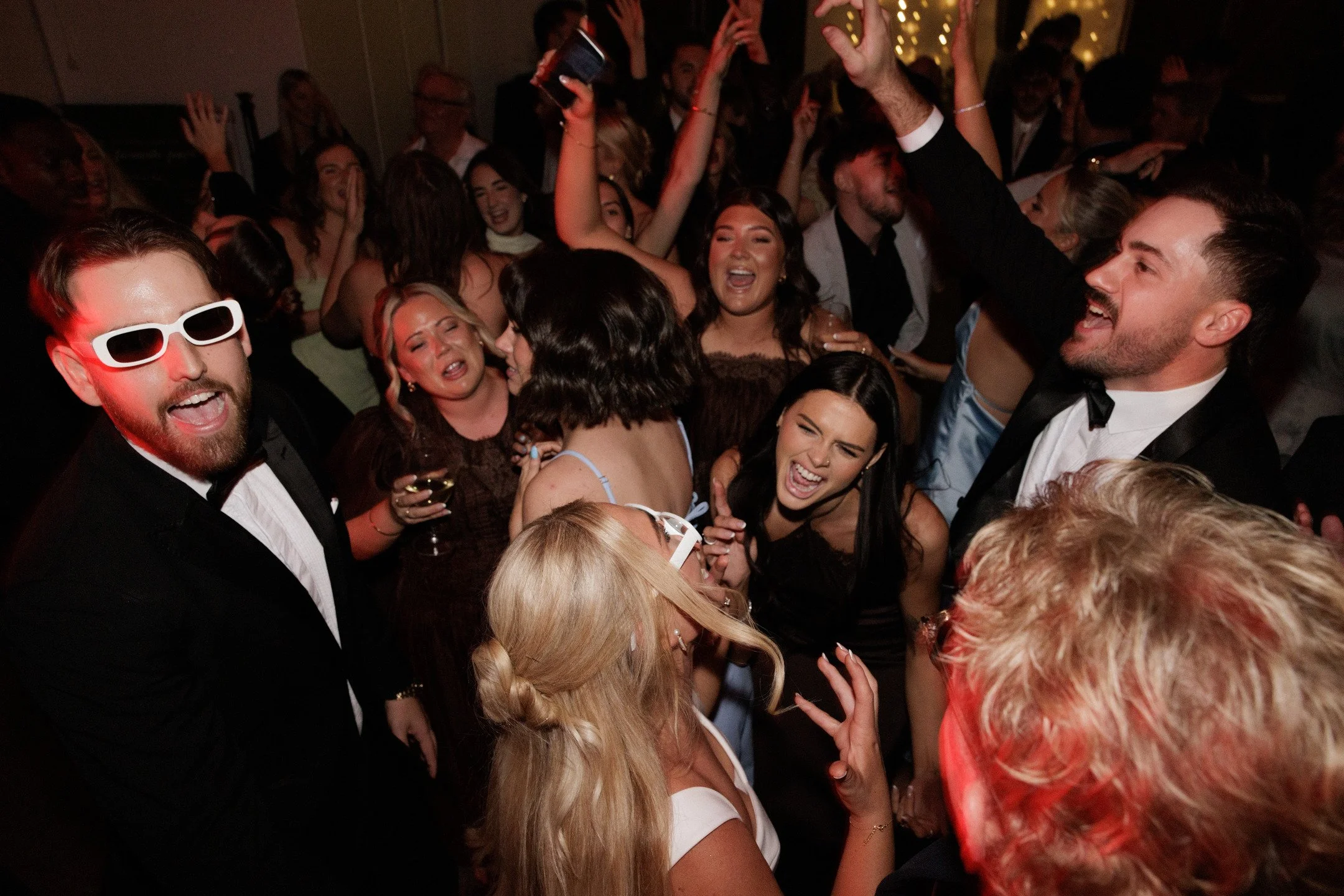 A lively crowd of people dancing and celebrating at a party or celebration, dressed in formal attire.