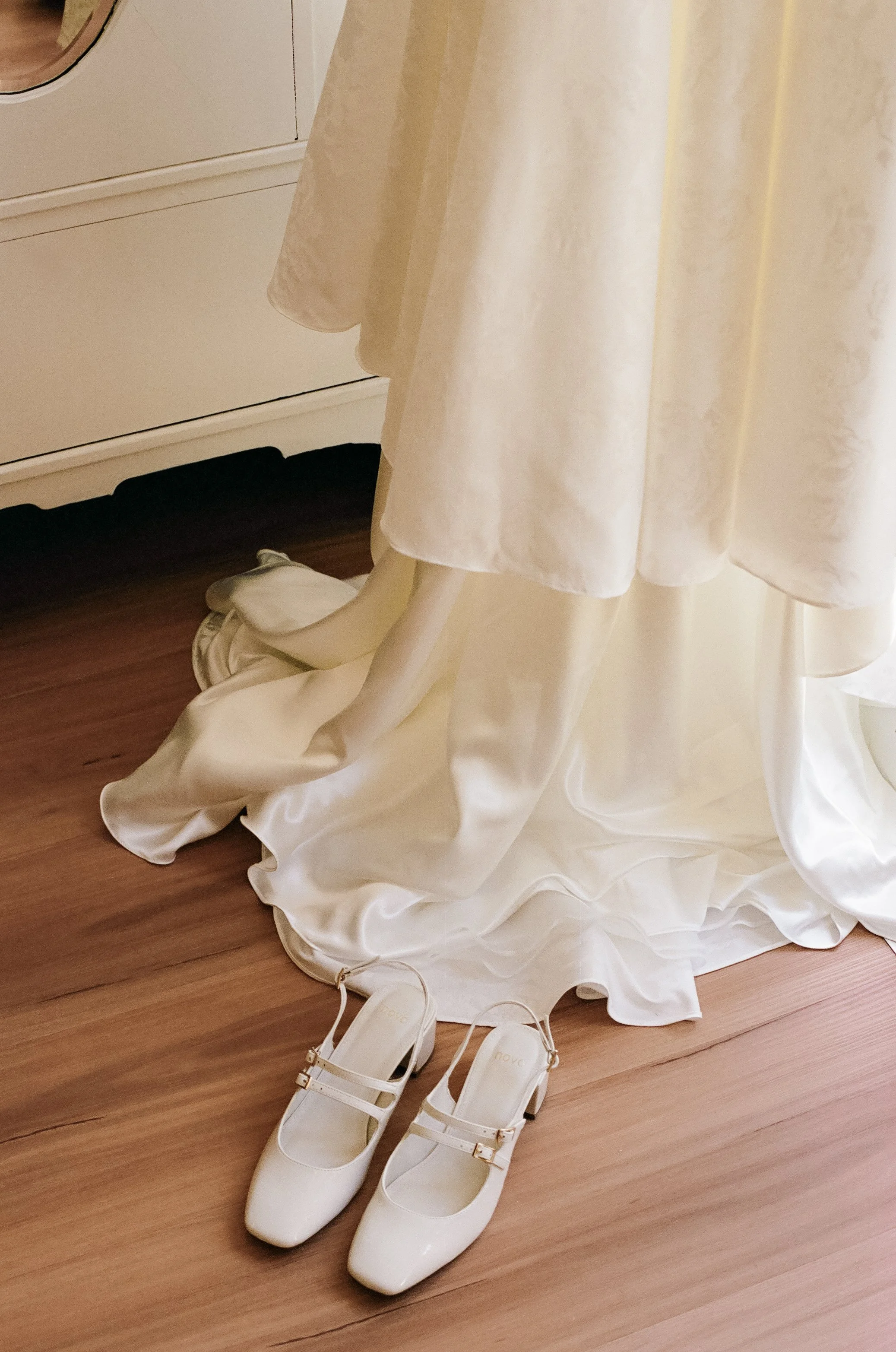 White wedding dress on a mannequin with a pair of white high-heeled shoes on the floor in front of it.