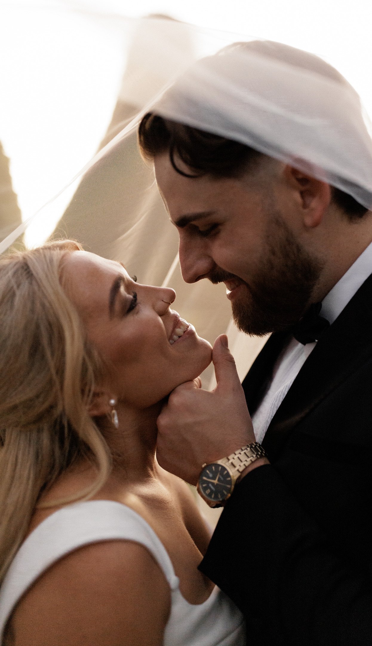 A happy couple on their wedding day sharing an intimate moment, with their foreheads touching and smiling at each other.