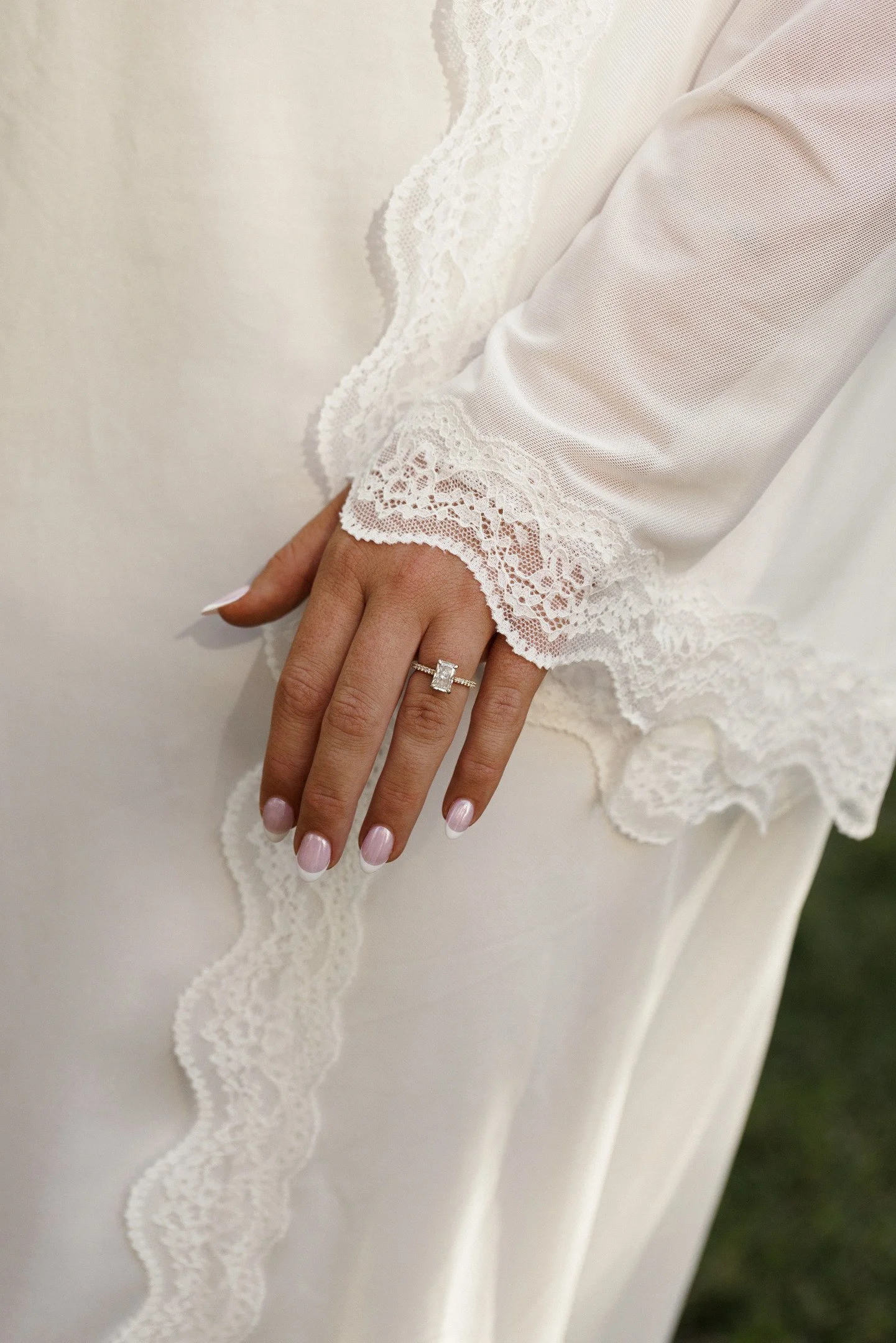 Close-up of a woman's hand with a wedding ring, resting on the lace detail of a white wedding dress.