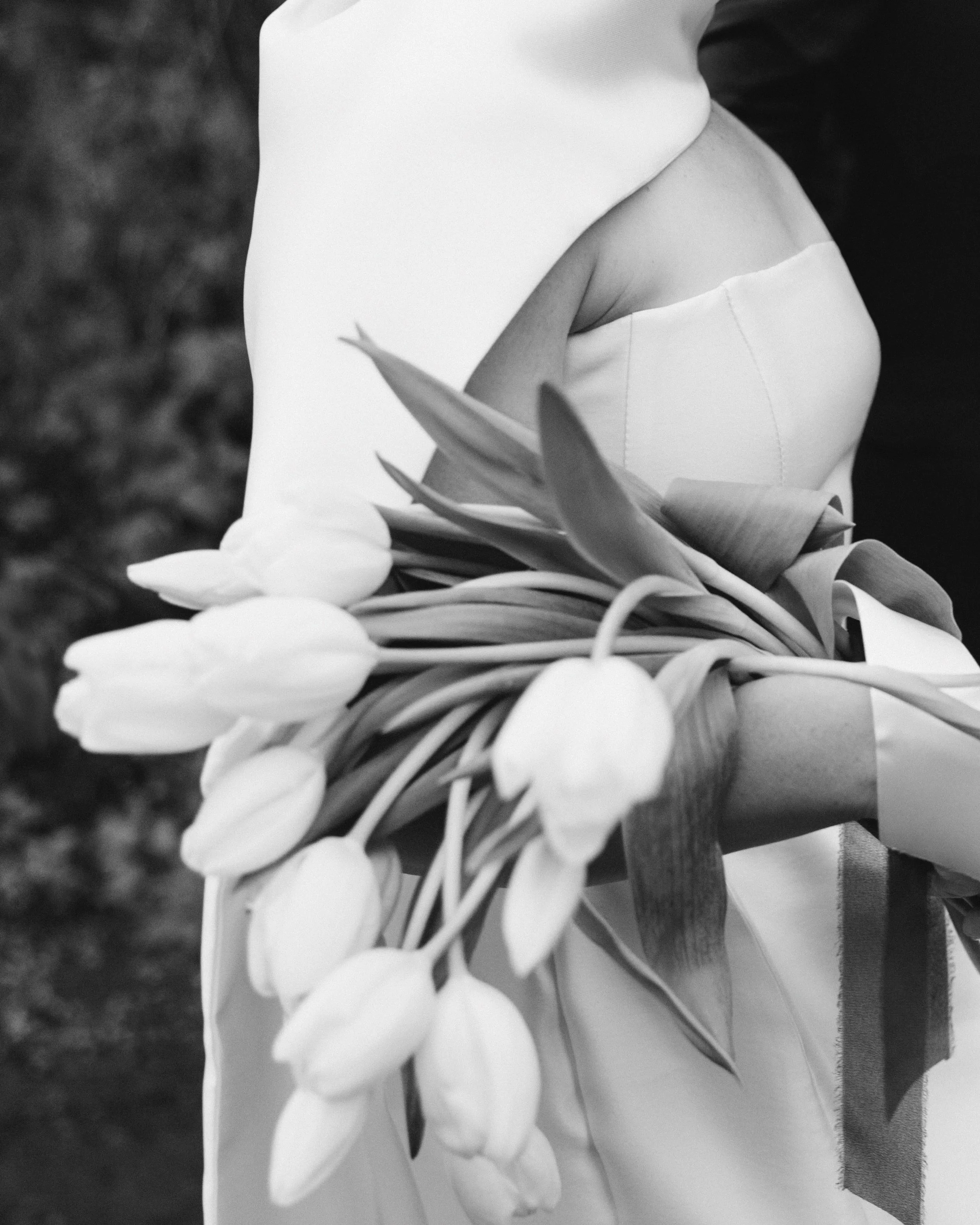 A person holding a bouquet of white tulips, wearing a white dress or gown, with a blurred outdoor background.