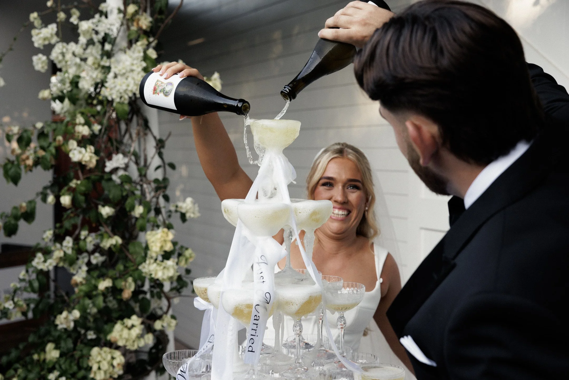 A man and a woman celebrate with champagne at a wedding or special event, pouring champagne into a tower of glasses