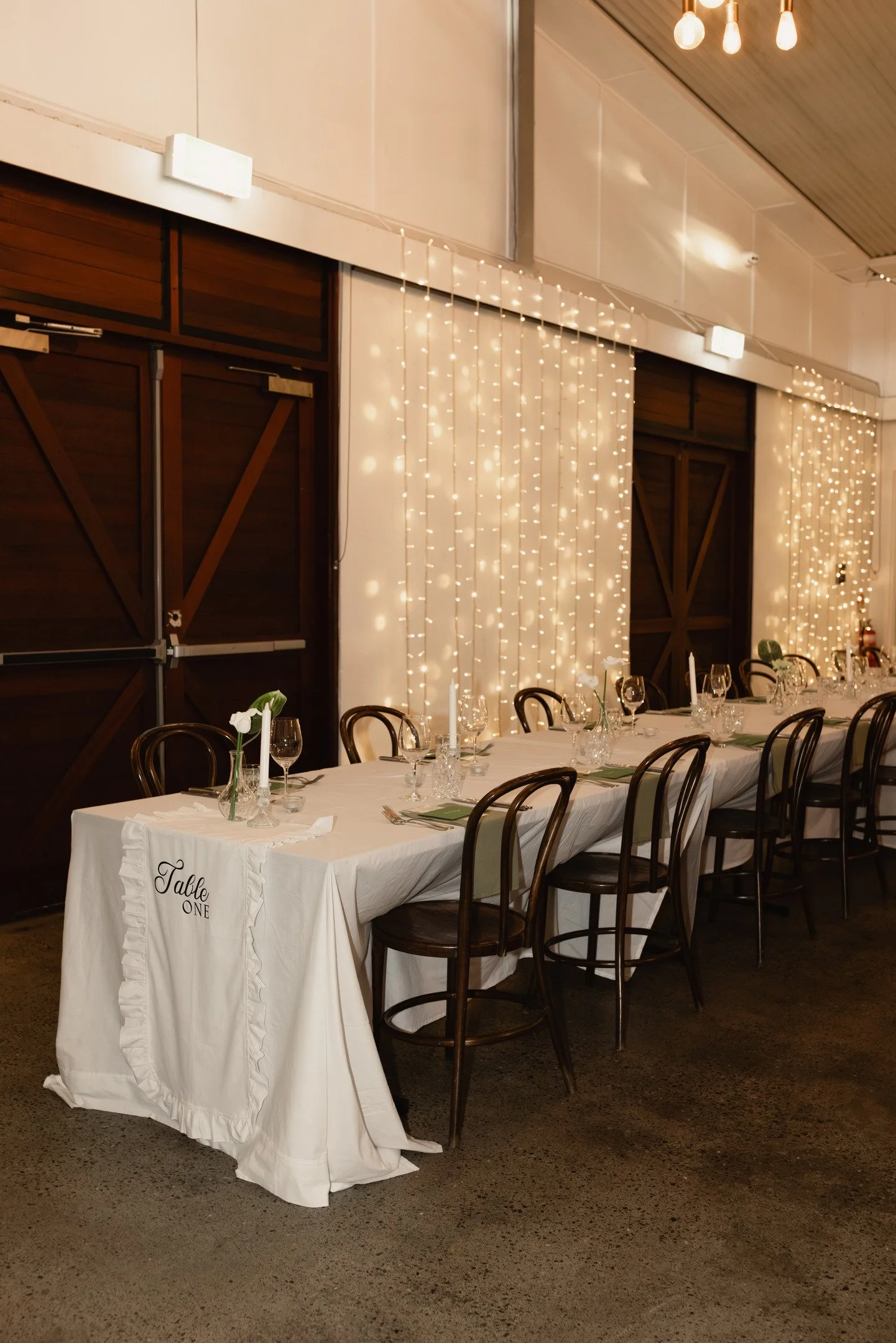 Decorated banquet hall with a long white dining table, black chairs, and string lights.