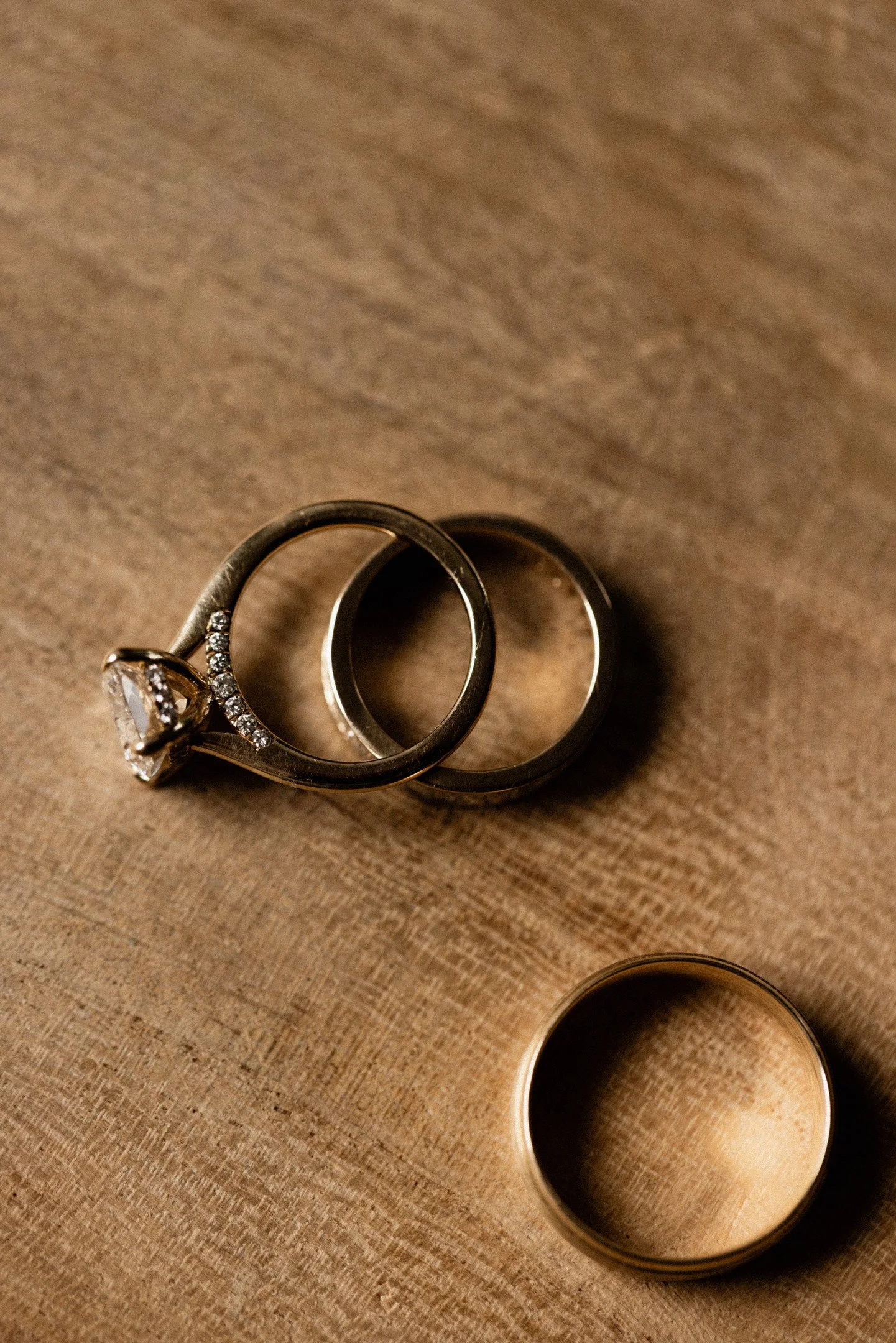 A close-up photo of two silver rings, one featuring a large central gemstone surrounded by smaller gemstones, and the other a plain band, lying on a wooden surface.