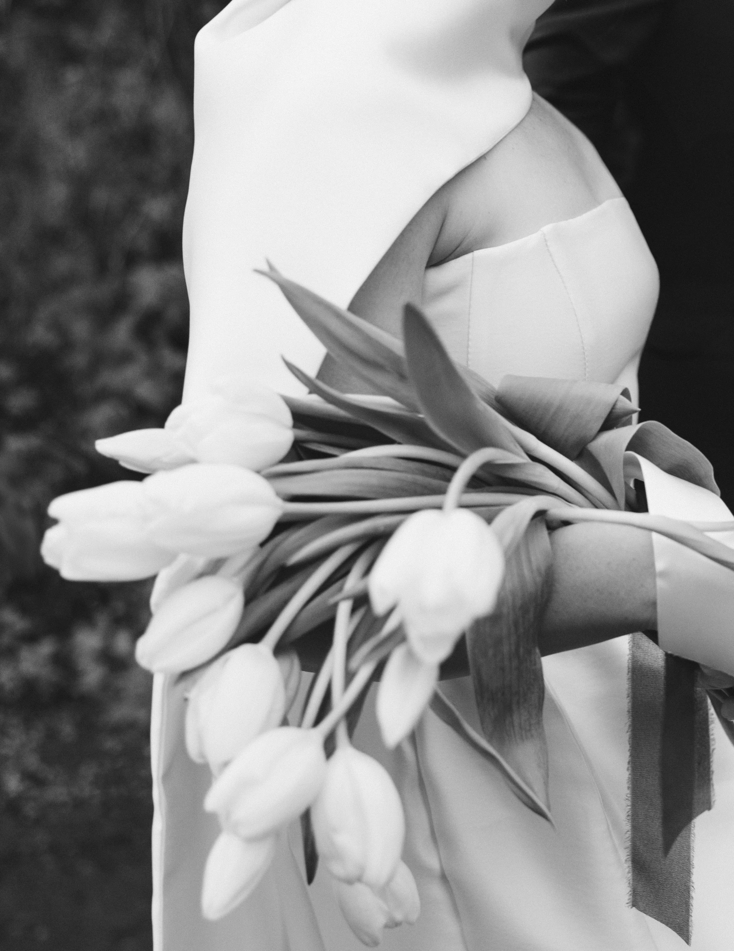 A person dressed in light-colored clothing holding a large bouquet of tulips and lilies. The photo is in black and white.