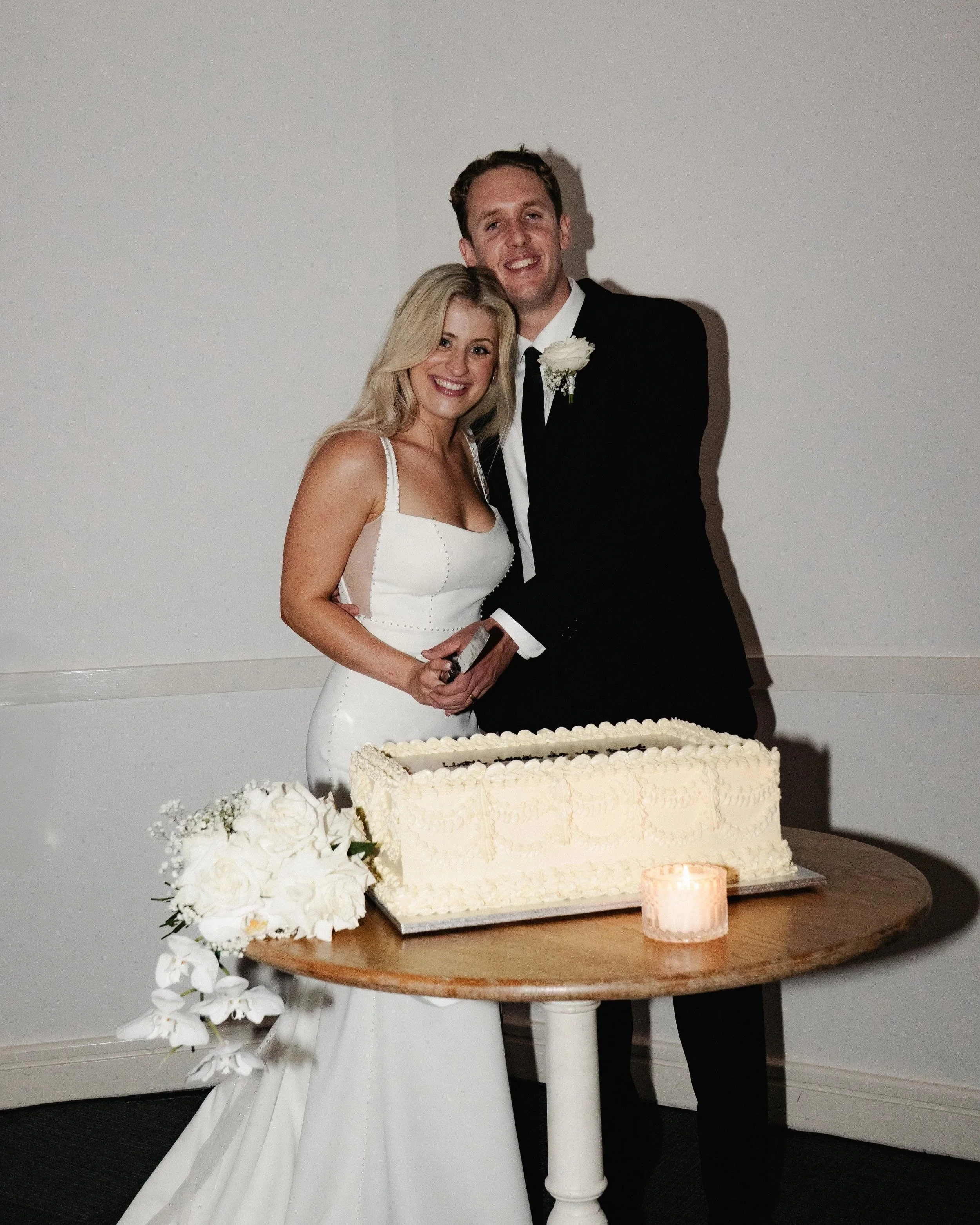 Bride and groom smiling while cutting wedding cake at a wedding reception.