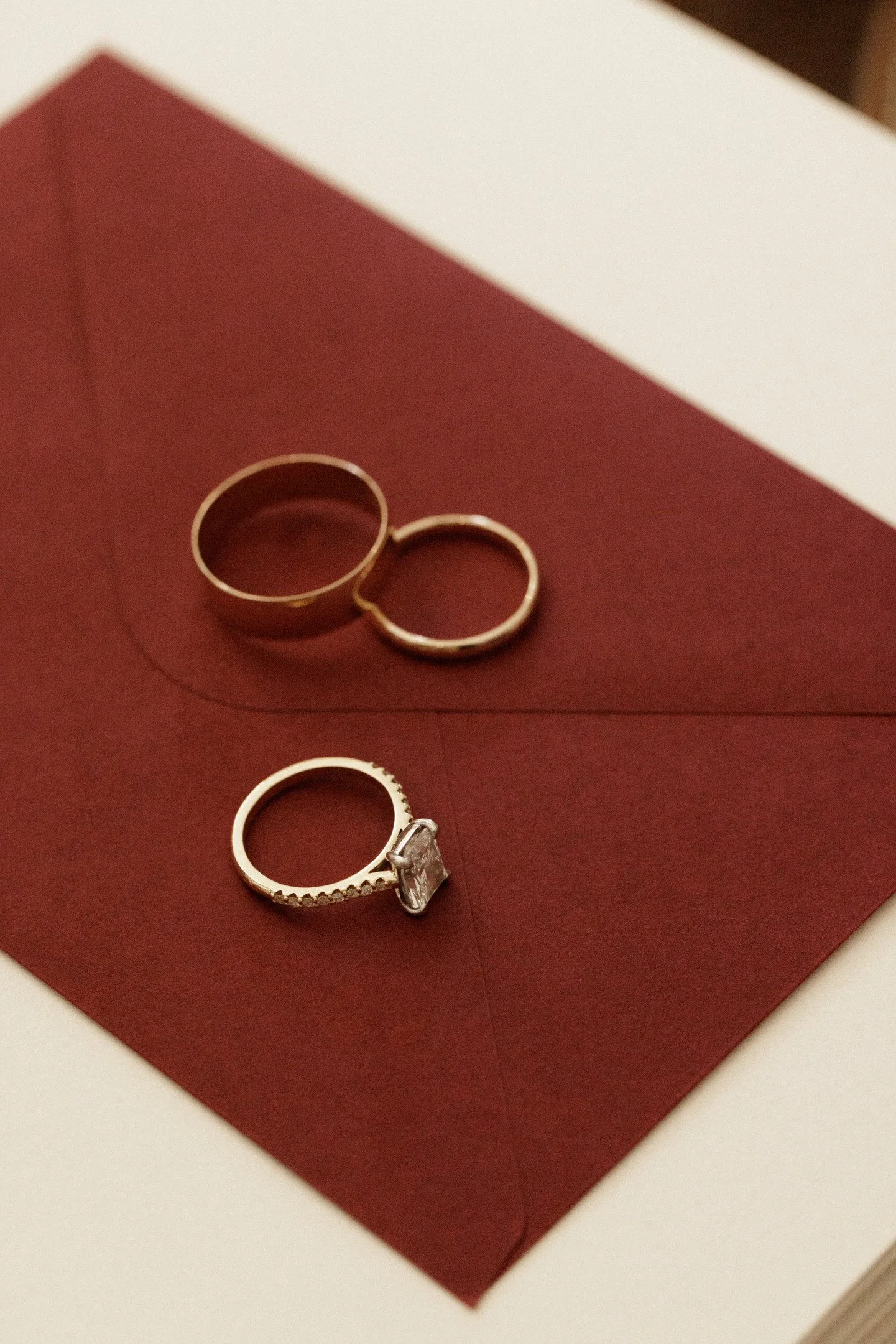 Three rings, one large with a stone and two smaller plain bands, placed on a red surface.