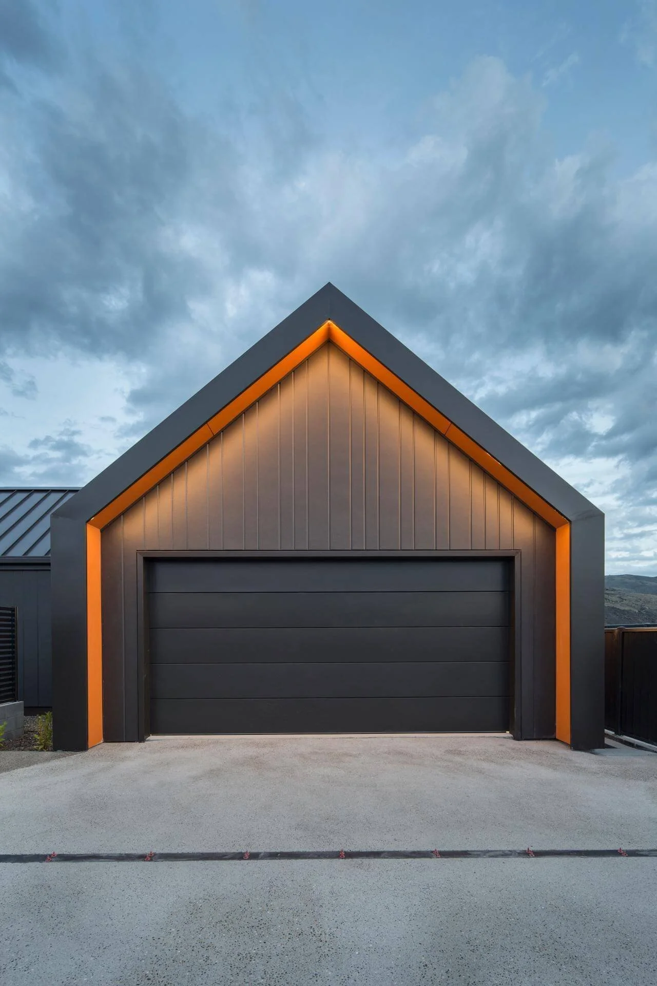 Modern garage with dark panels and orange trim in an A-frame design against a cloudy sky.