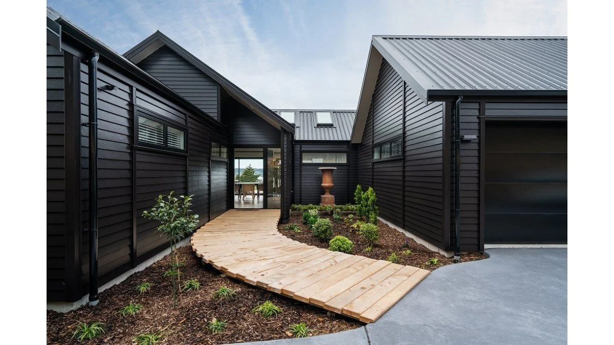 Modern black house exterior with wooden walkway and landscaped garden