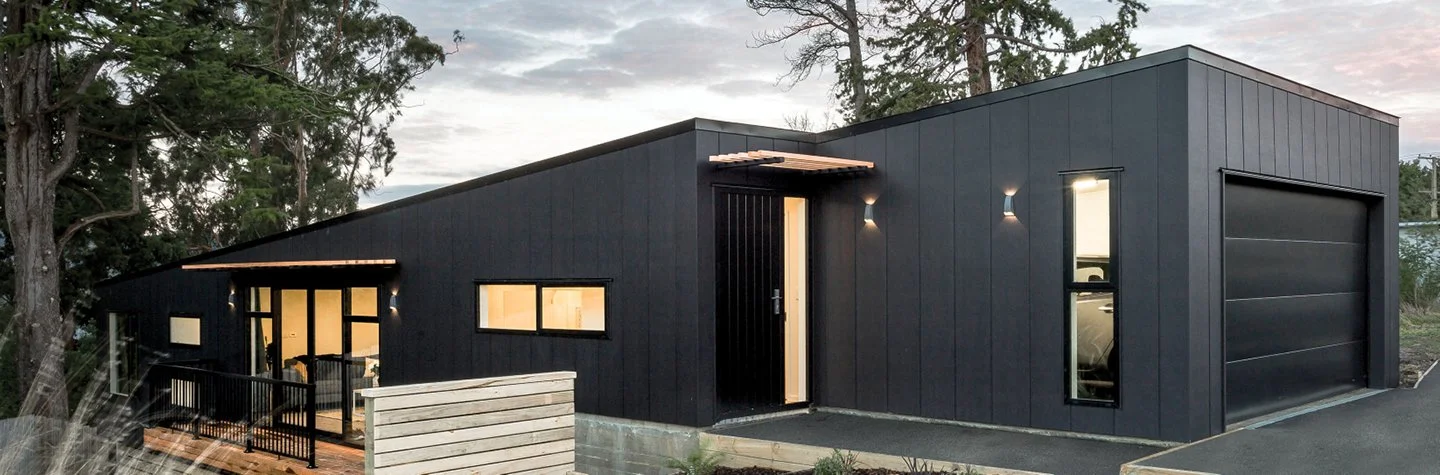Modern black house with asymmetrical design, featuring large windows and an attached garage.