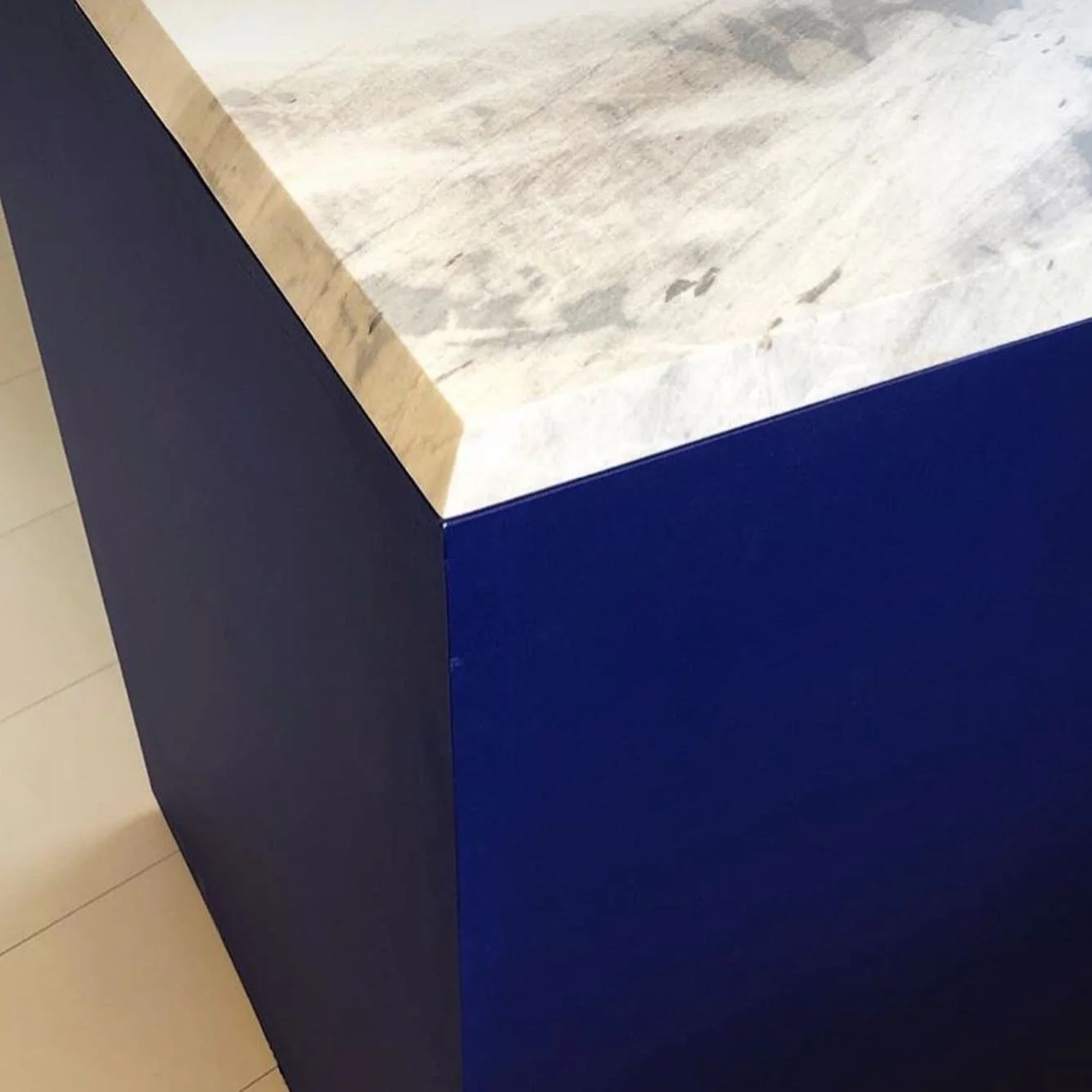 Close-up of a corner of a piece of furniture with a marble top and navy blue sides.