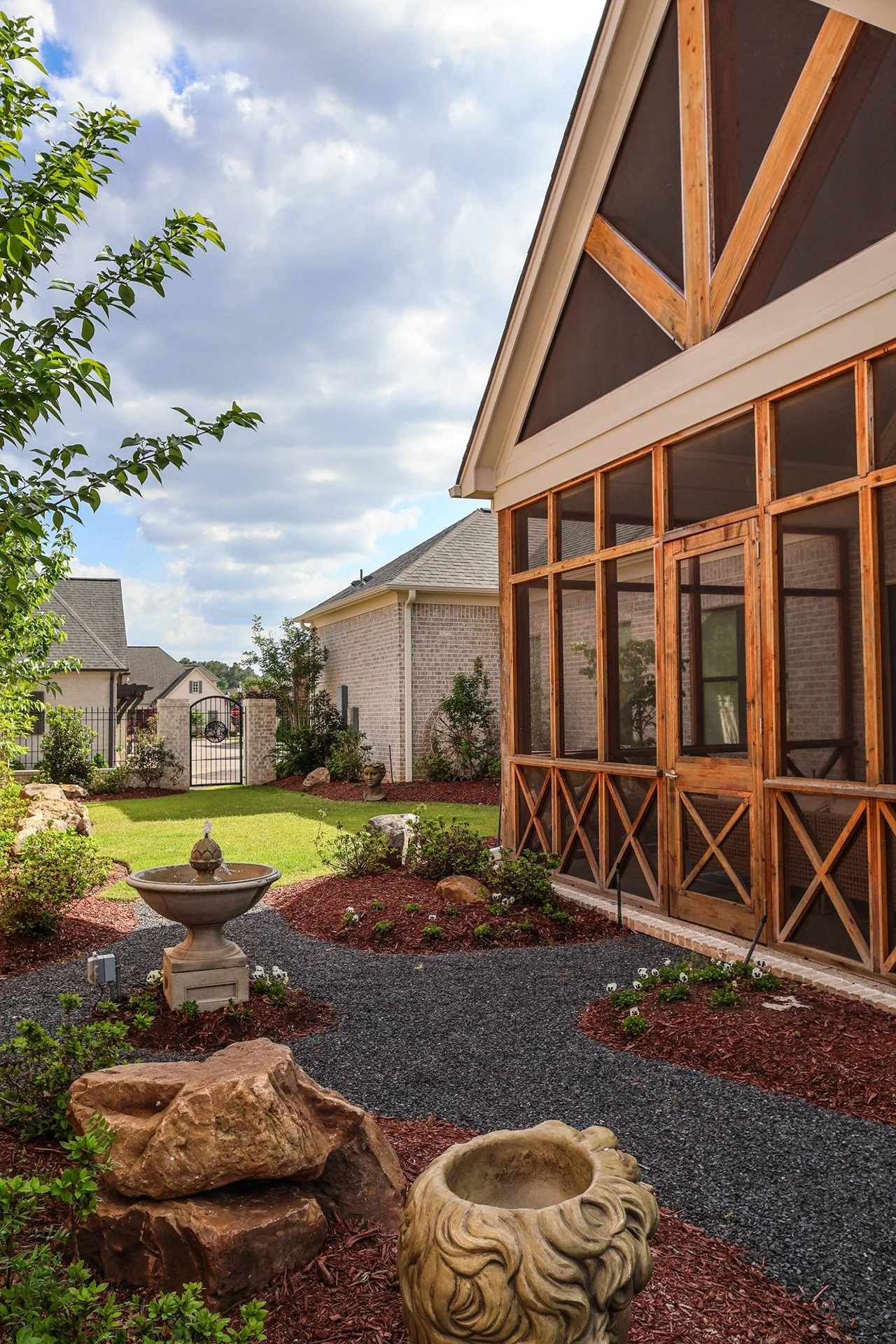 mesh and natural wood enclosed sunroom with garden gravel trail around water fountain