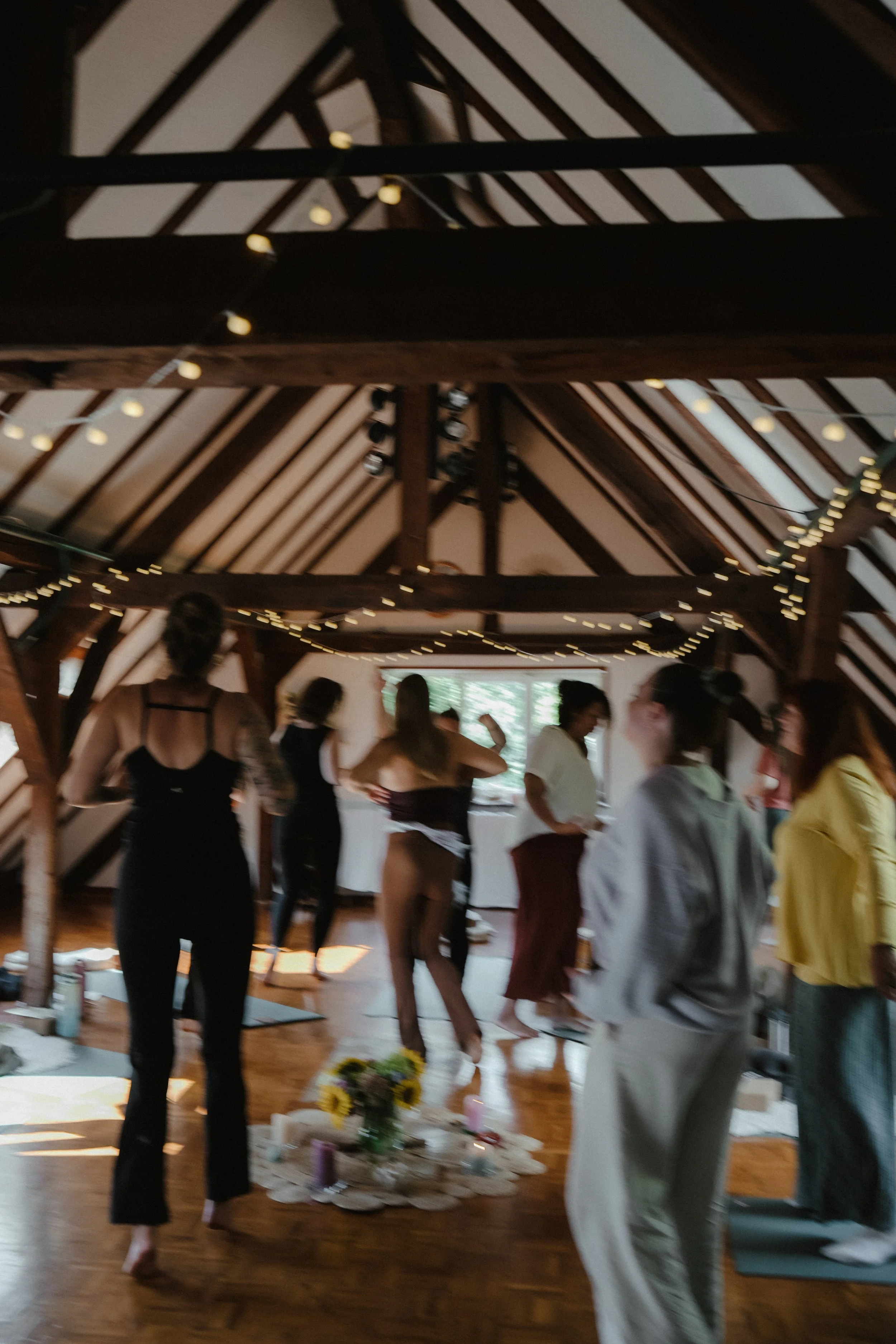 Menschen im Brautkleid und Anzug, die an einer Hochzeit im Innenraum einer Holzbarn-Location teilnehmen, mit Dekorationen und Blumen.