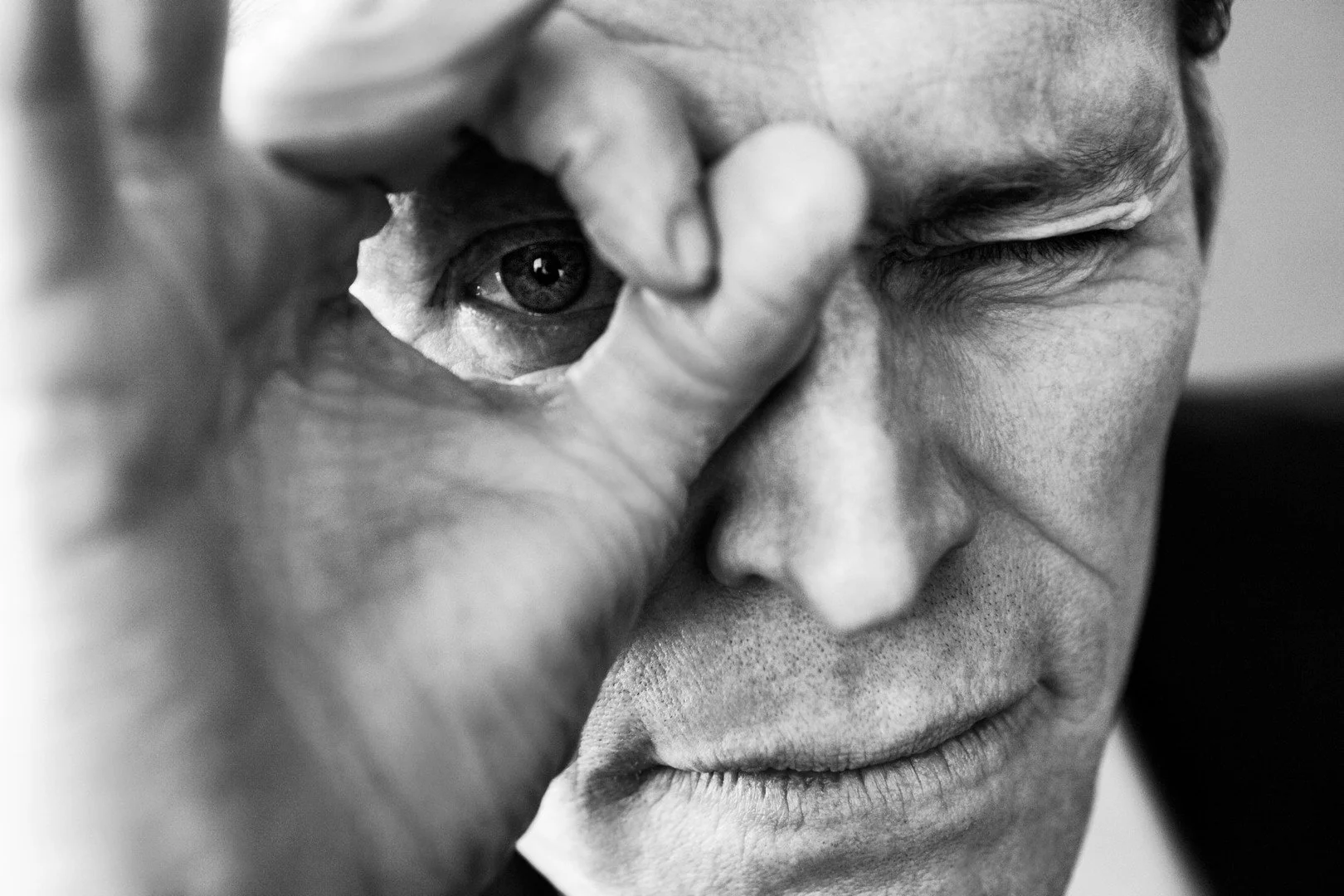 A black and white close-up photo of a person's face with their eye open, looking through a small circle made with their hand.