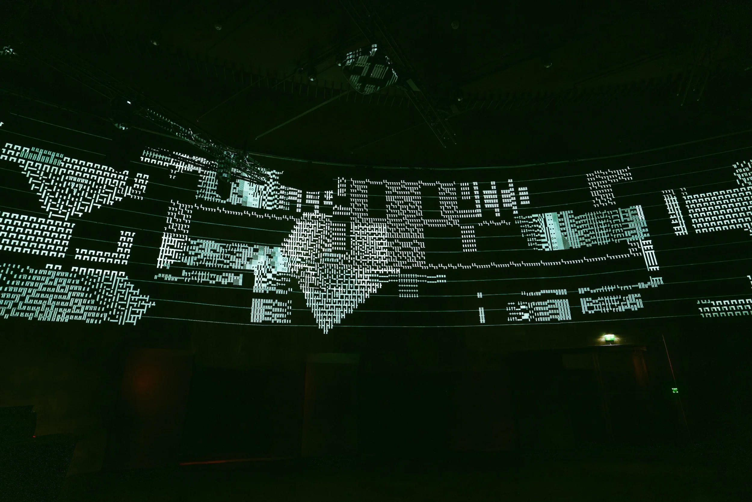 Large digital display screen with a pixelated map of the world in bright white lines on a dark background, resembling a digital or technological theme.