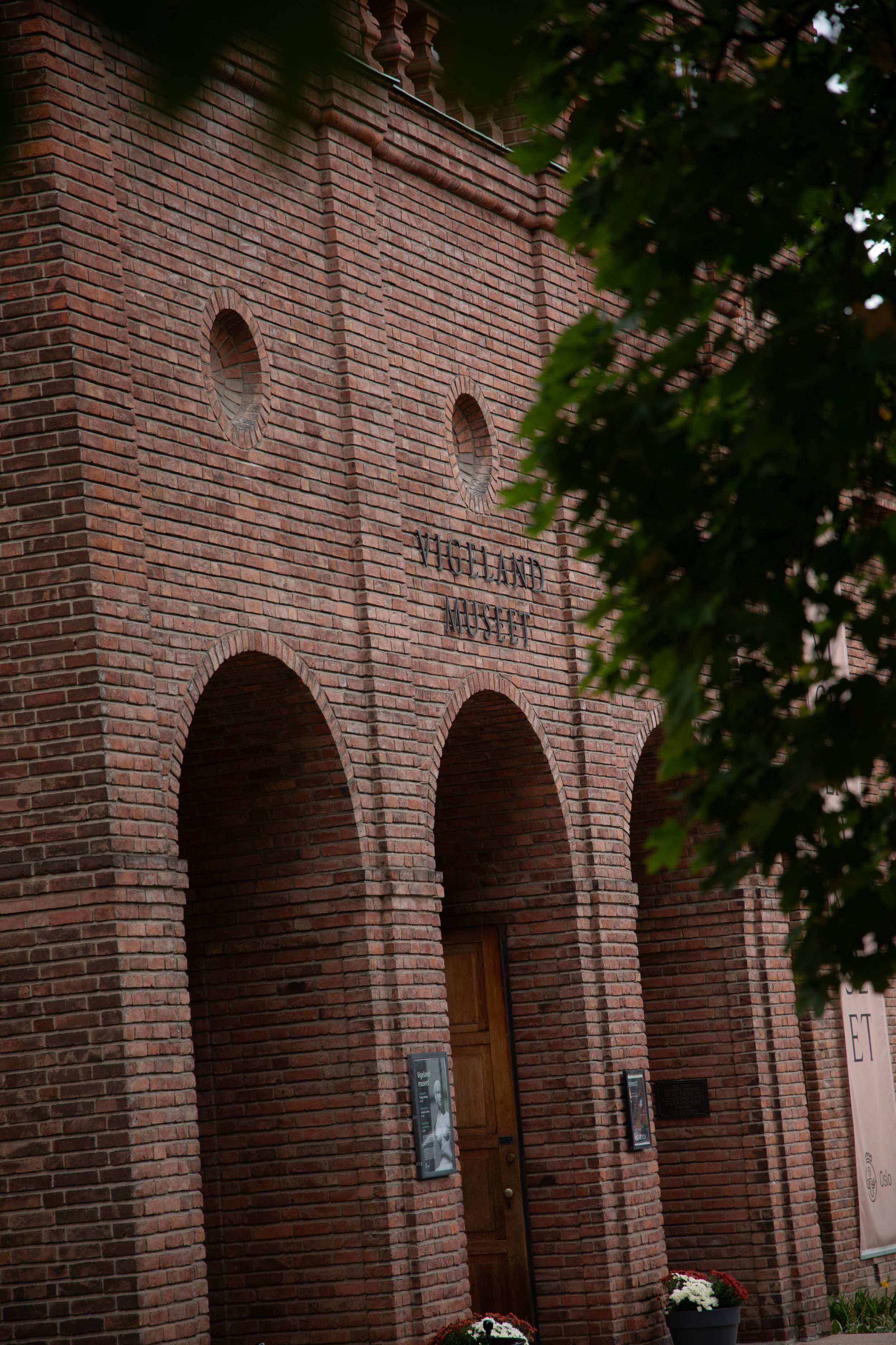 The Highland Museum building made of red brick with three arches at the entrance, surrounded by greenery and flower pots.