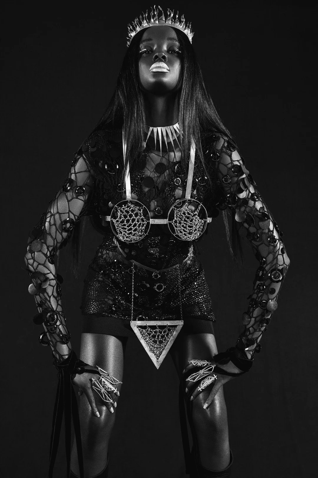 A woman wearing a crown, jewelry, and intricate fashion in black and white photoshoot.