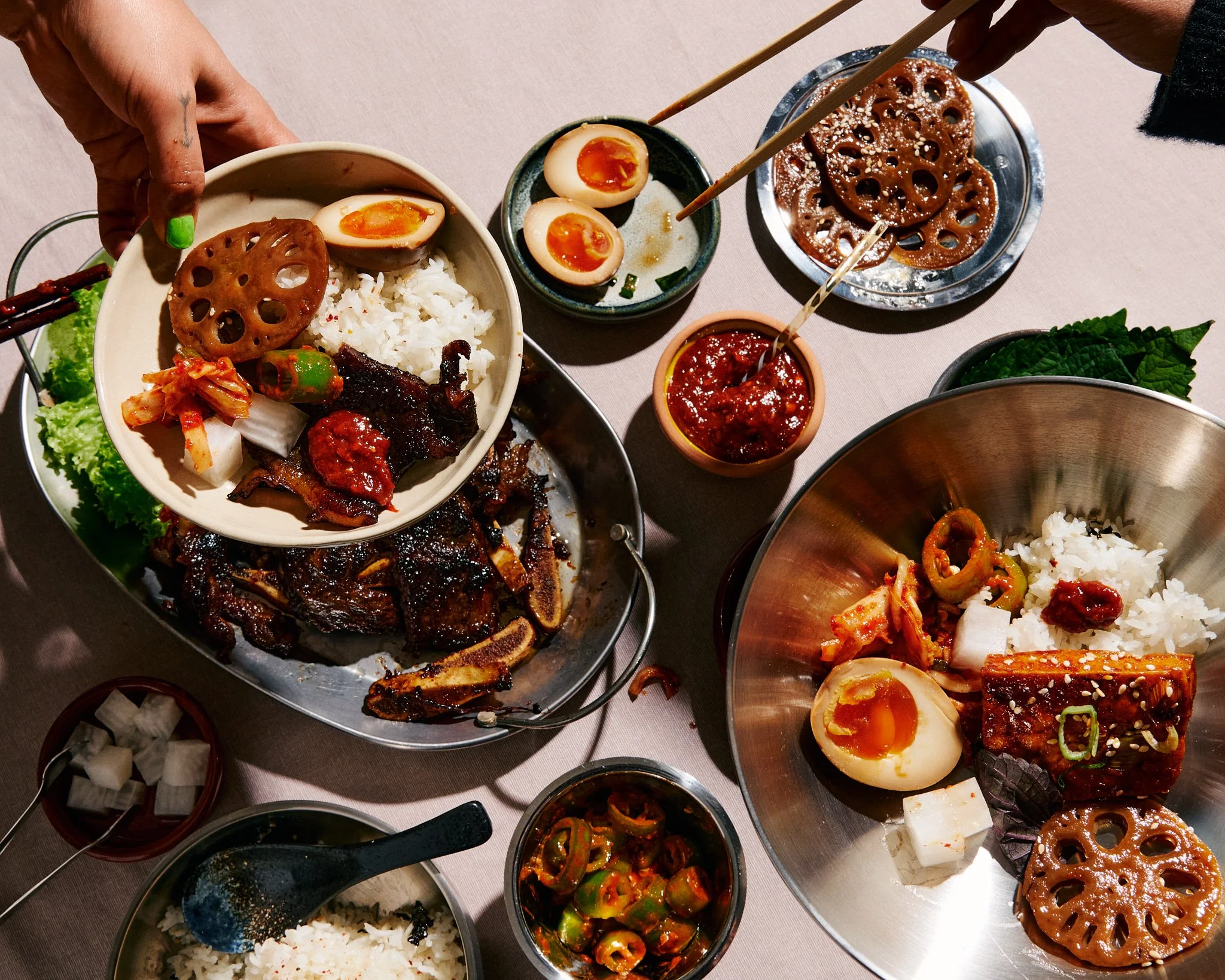 A variety of Korean dishes on a table, including rice, boiled eggs, grilled meat, kimchi, lotus root, and assorted vegetables.