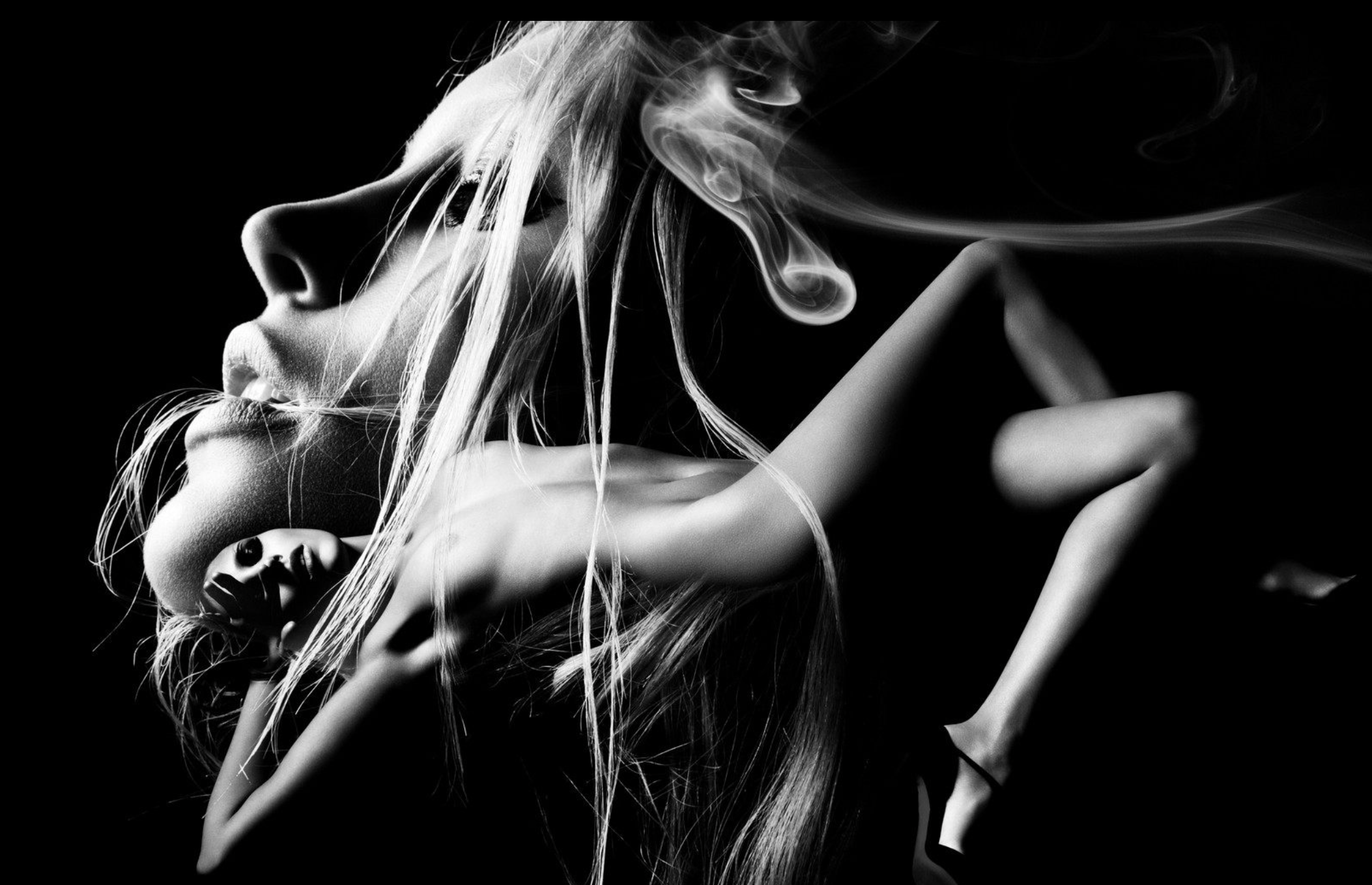 Black and white artistic photo of a woman with long hair, eyes closed, smoking, with smoke swirling around her head, and her hand touching her face and hair.