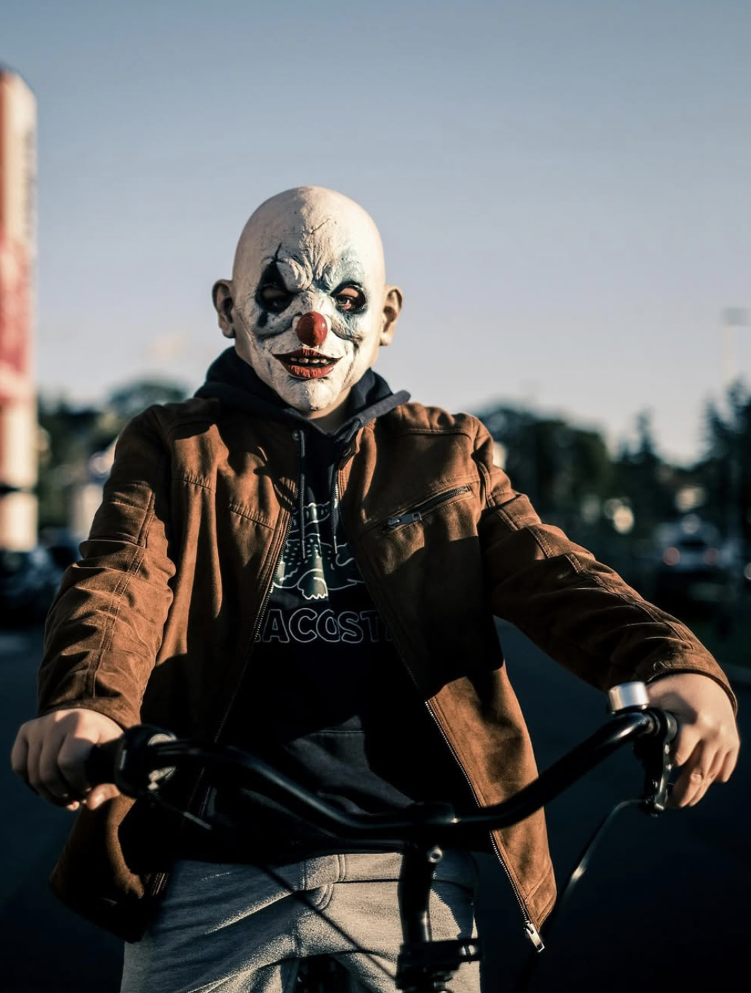 A person wearing a clown mask riding a bicycle outdoors during daylight.