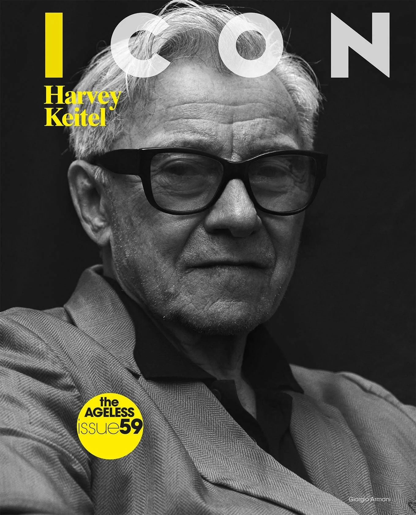 Black and white portrait of an older man wearing glasses, with white hair, dressed in a patterned jacket and black shirt, on the cover of a magazine. The magazine features the titles 'ICON' and 'Harvey Keitel,' and a yellow circle with the text 'the AGELESS issue 59.'