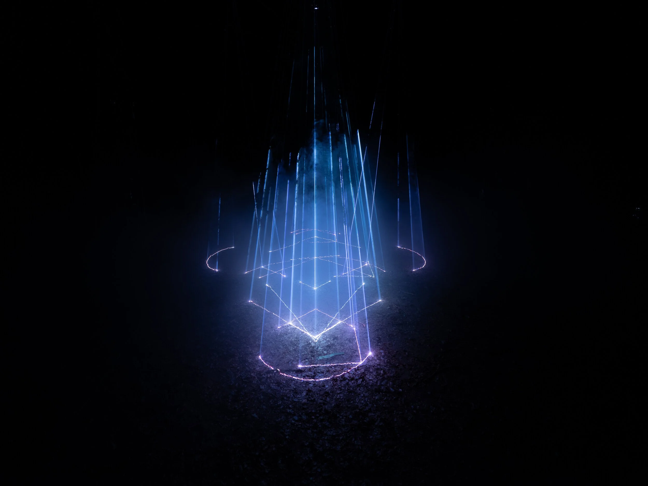 Blue laser light display projected onto the ground in a circular pattern in a dark environment.