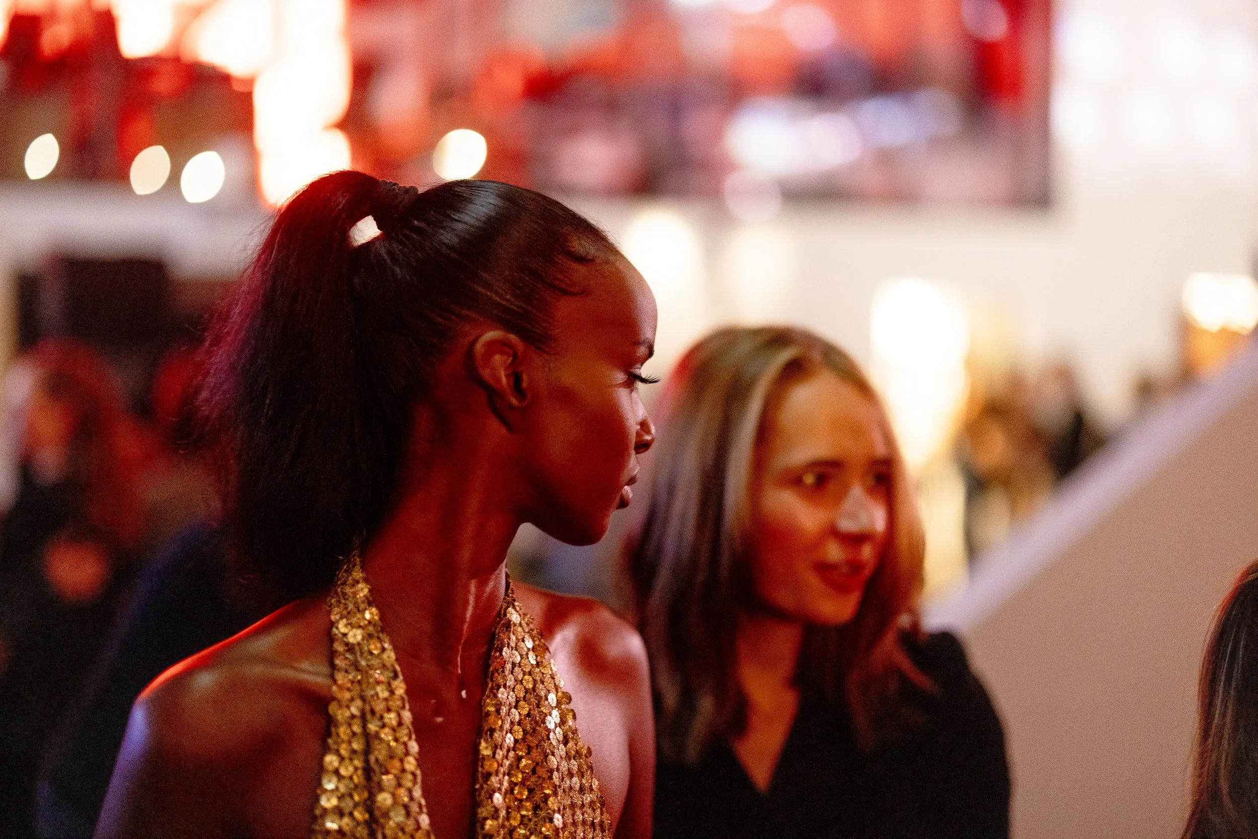 Two women talking at a social event with blurred background lighting
