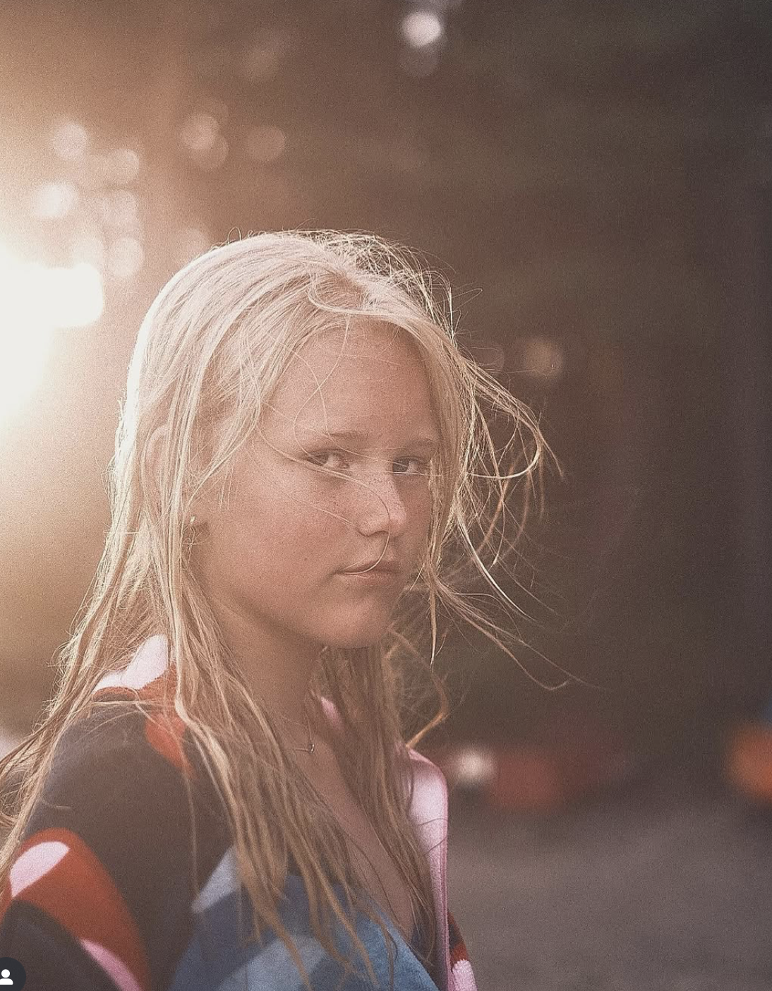 A young woman with wet blonde hair looking over her shoulder, illuminated by a warm light source behind her.