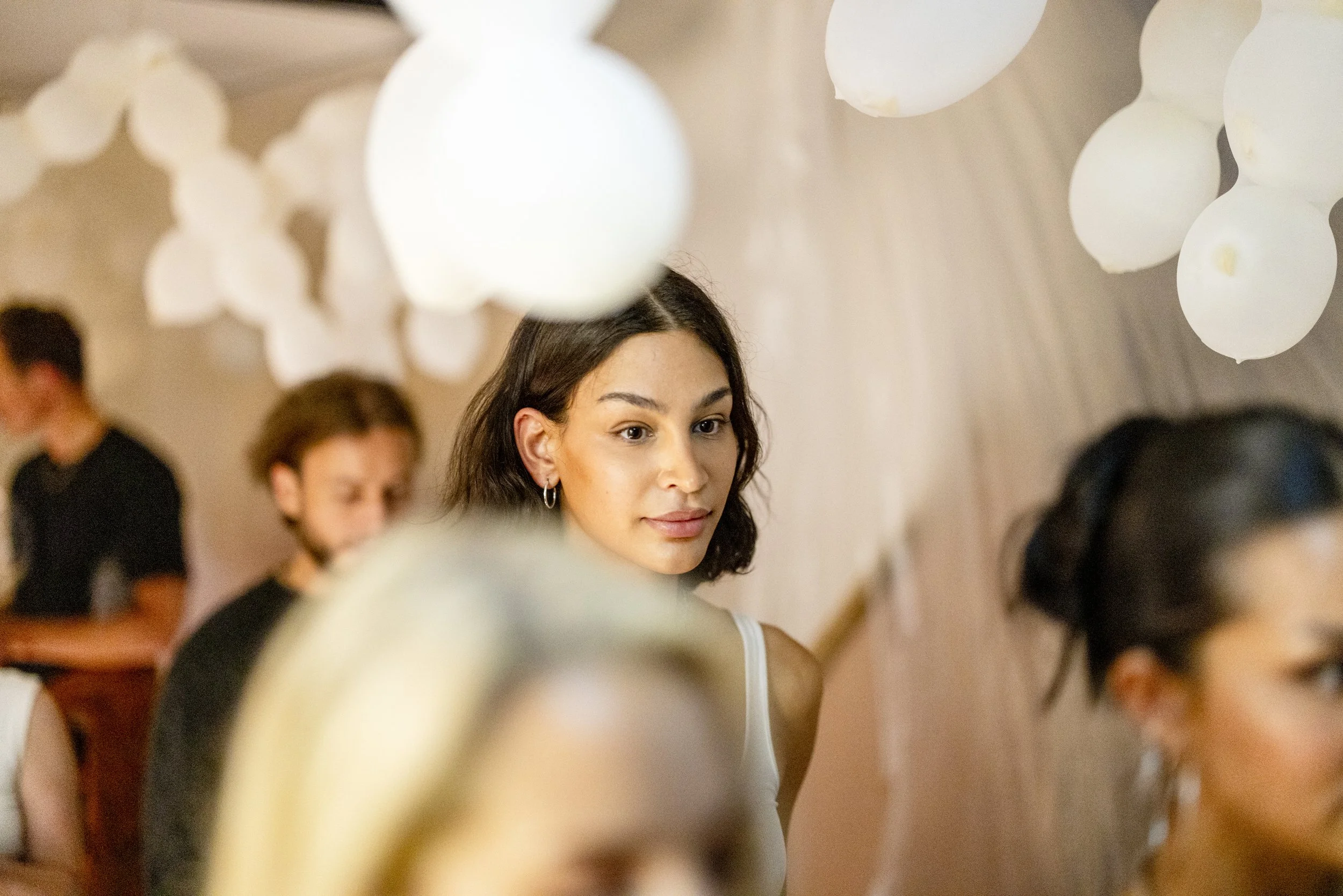 A woman with shoulder-length dark hair and earrings looking to the side at an indoor social gathering.