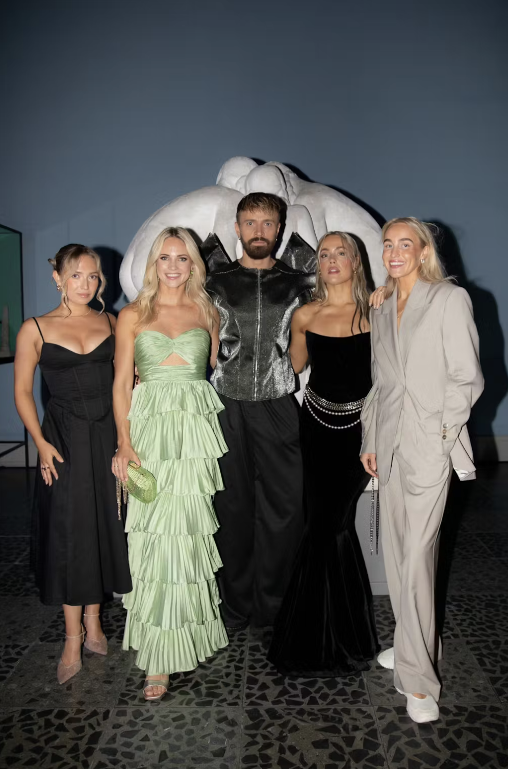 Group of five people posing in front of a large animal sculpture at an art exhibit.