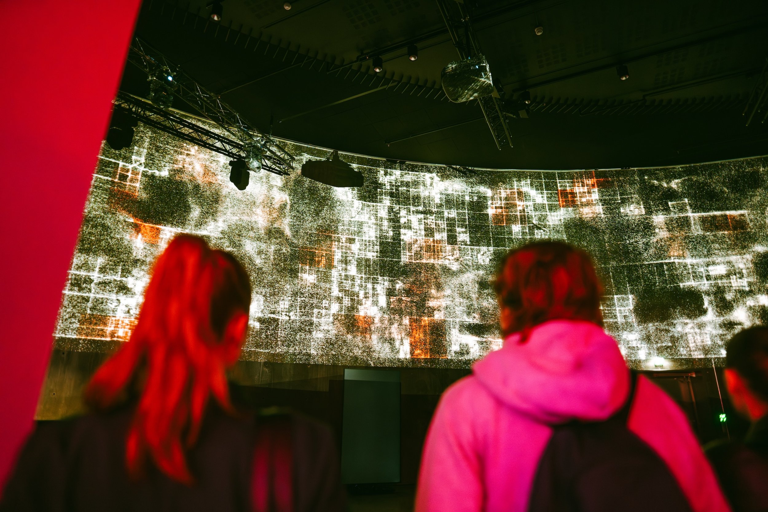 People watching a digital art installation projected on a curved wall in a dark room.