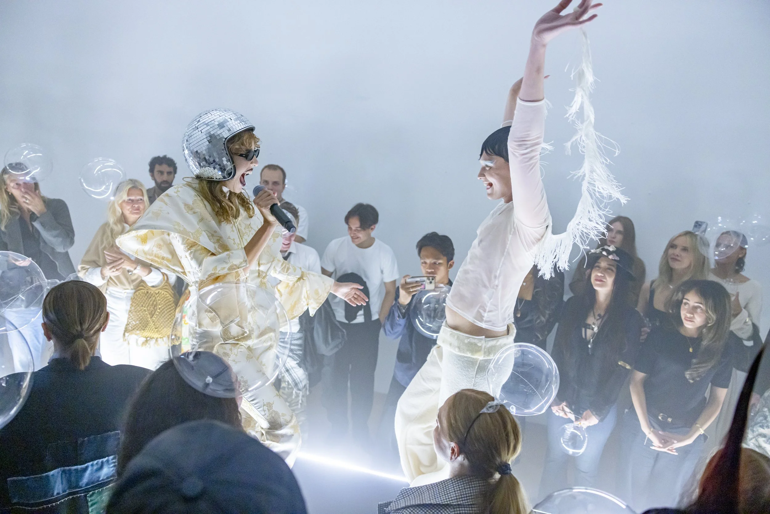 People dancing and singing at a lively party or celebration with balloons and disco balls.