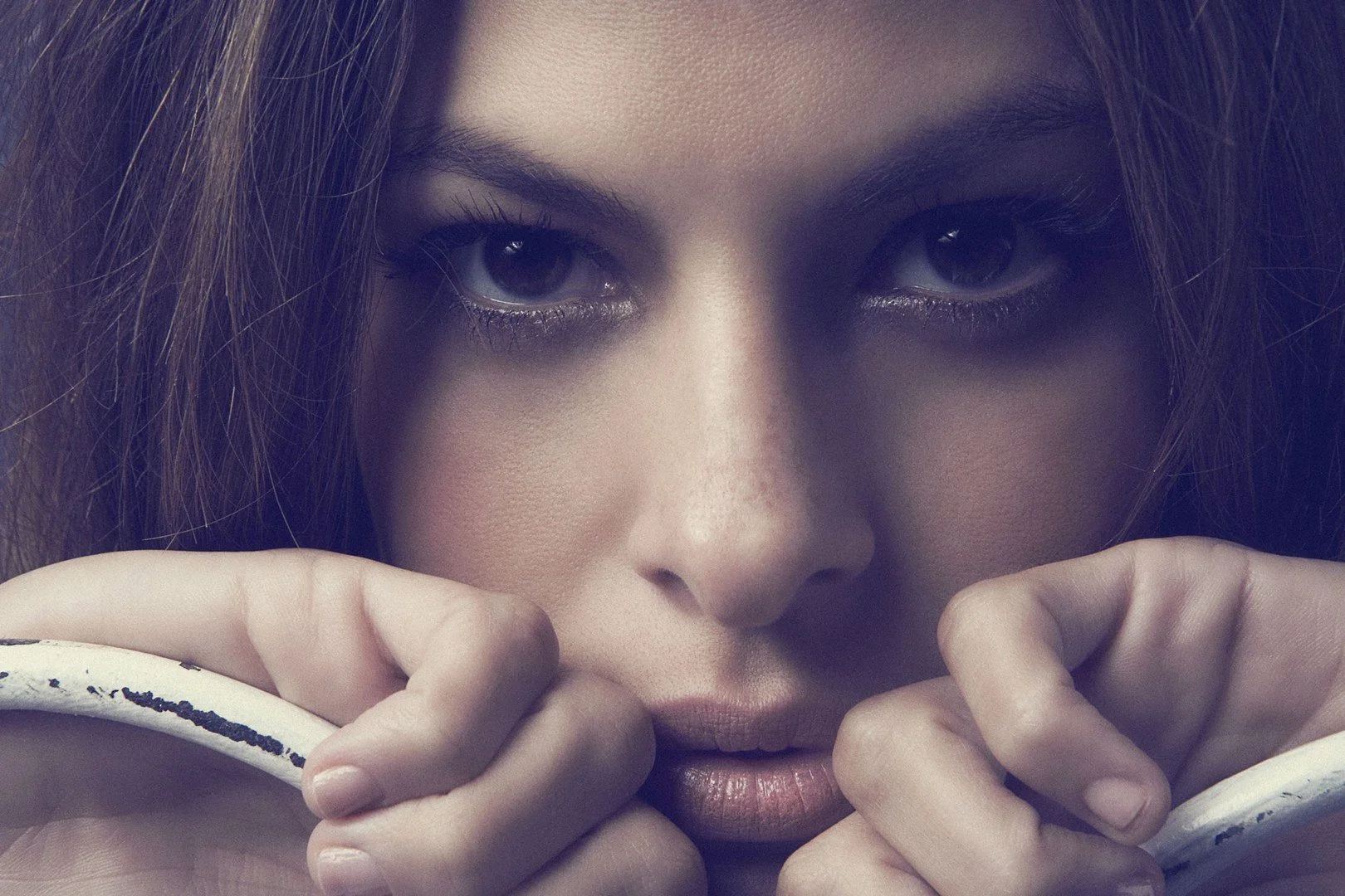 Close-up of a woman with intense eyes holding a white object near her face.