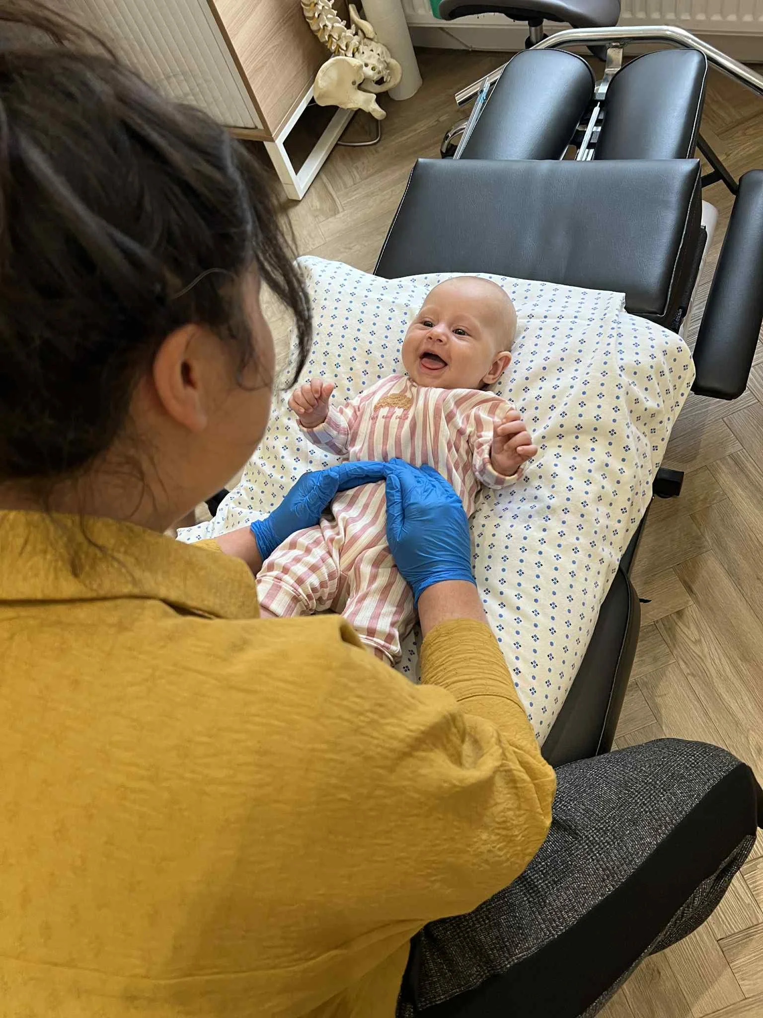 Our Chiropractor in Kettering,  in a yellow shirt,  examining a smiling baby on Chiropractic table.
