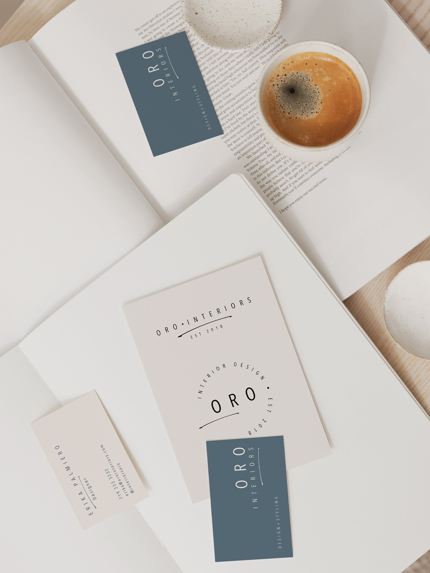 Open magazine or brochure displaying branding for 'ORO Interiors,' with minimalistic black and white design, and a cup of coffee with foam on top placed on the magazine.