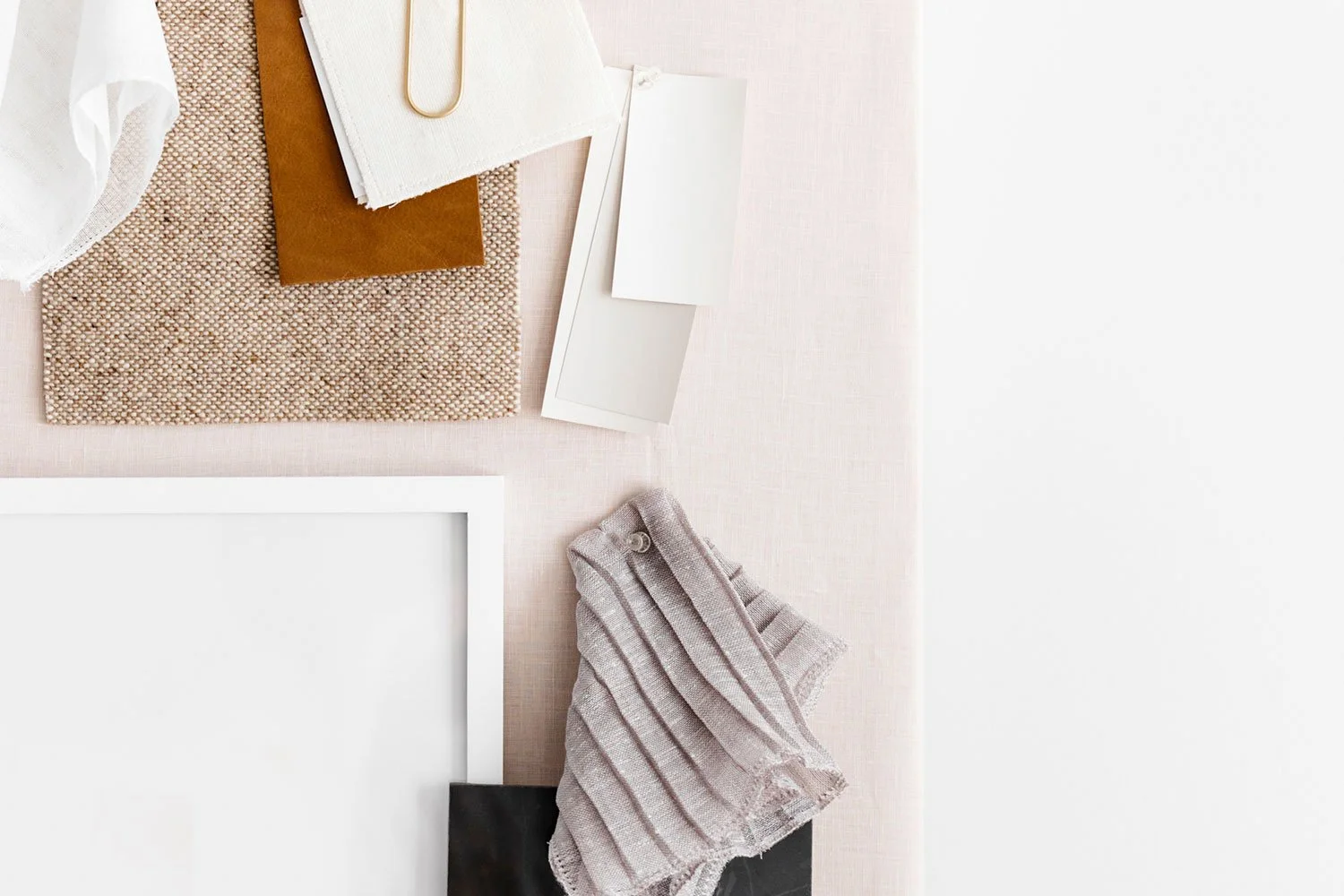 Flat lay of office or craft desk with various paper samples, a fabric swatch, a tissue, a clipboard, a paperclip, framed artwork, and a cloth napkin or towel.
