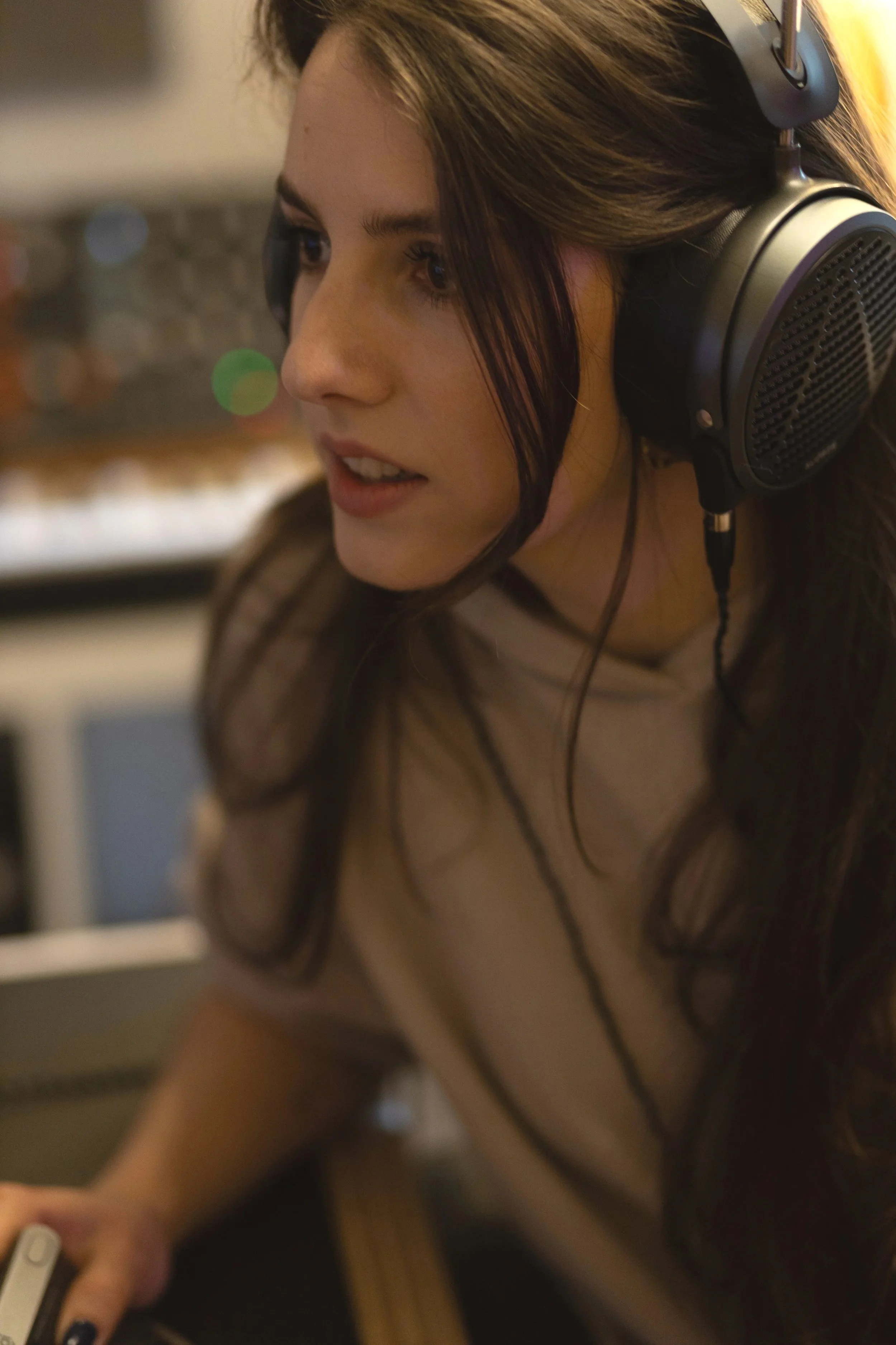 A woman wearing large headphones while working on a computer in a dimly lit room.