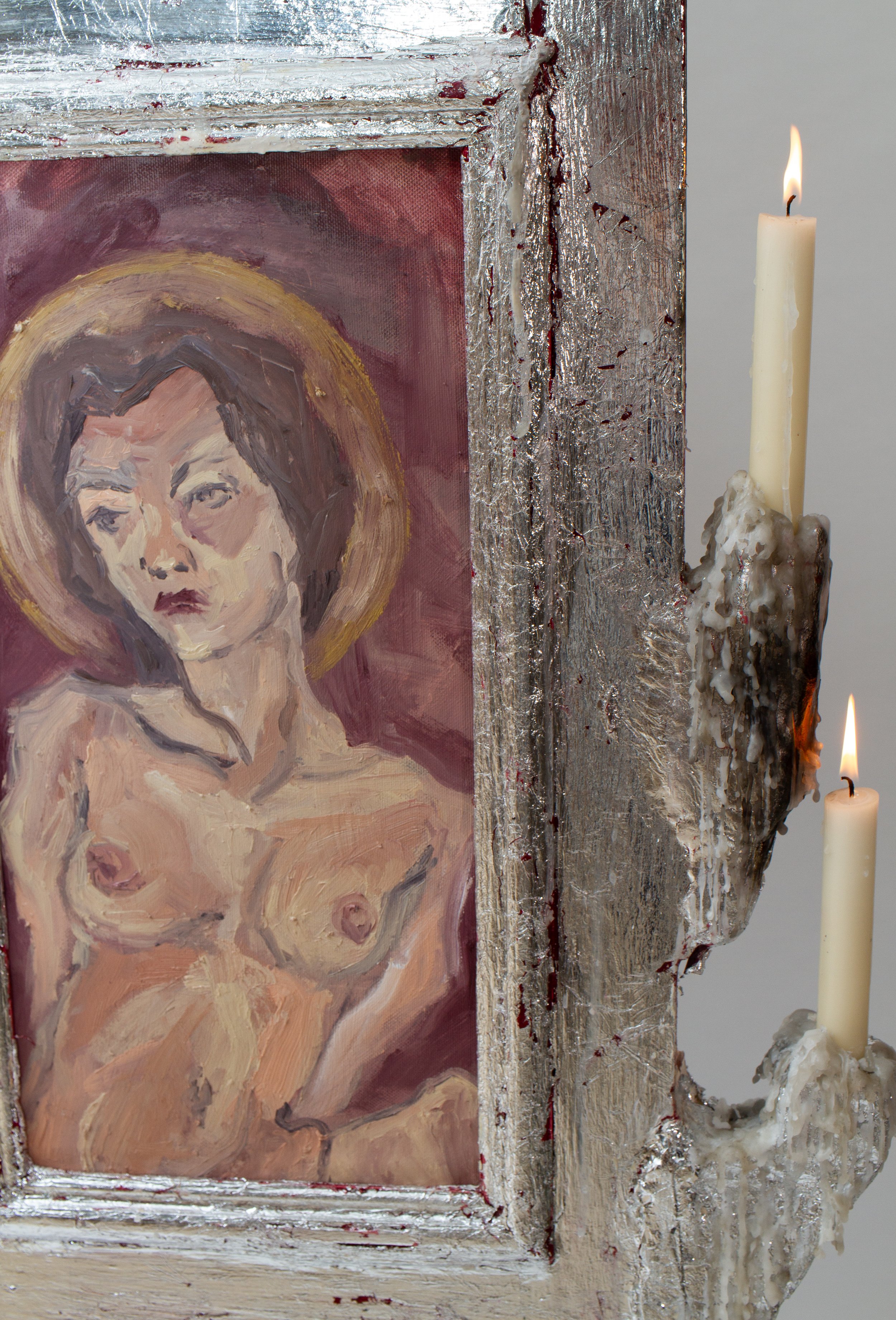 A framed painting of a woman with dark hair and a halo, with a candle attached to the side of the frame and melting wax.