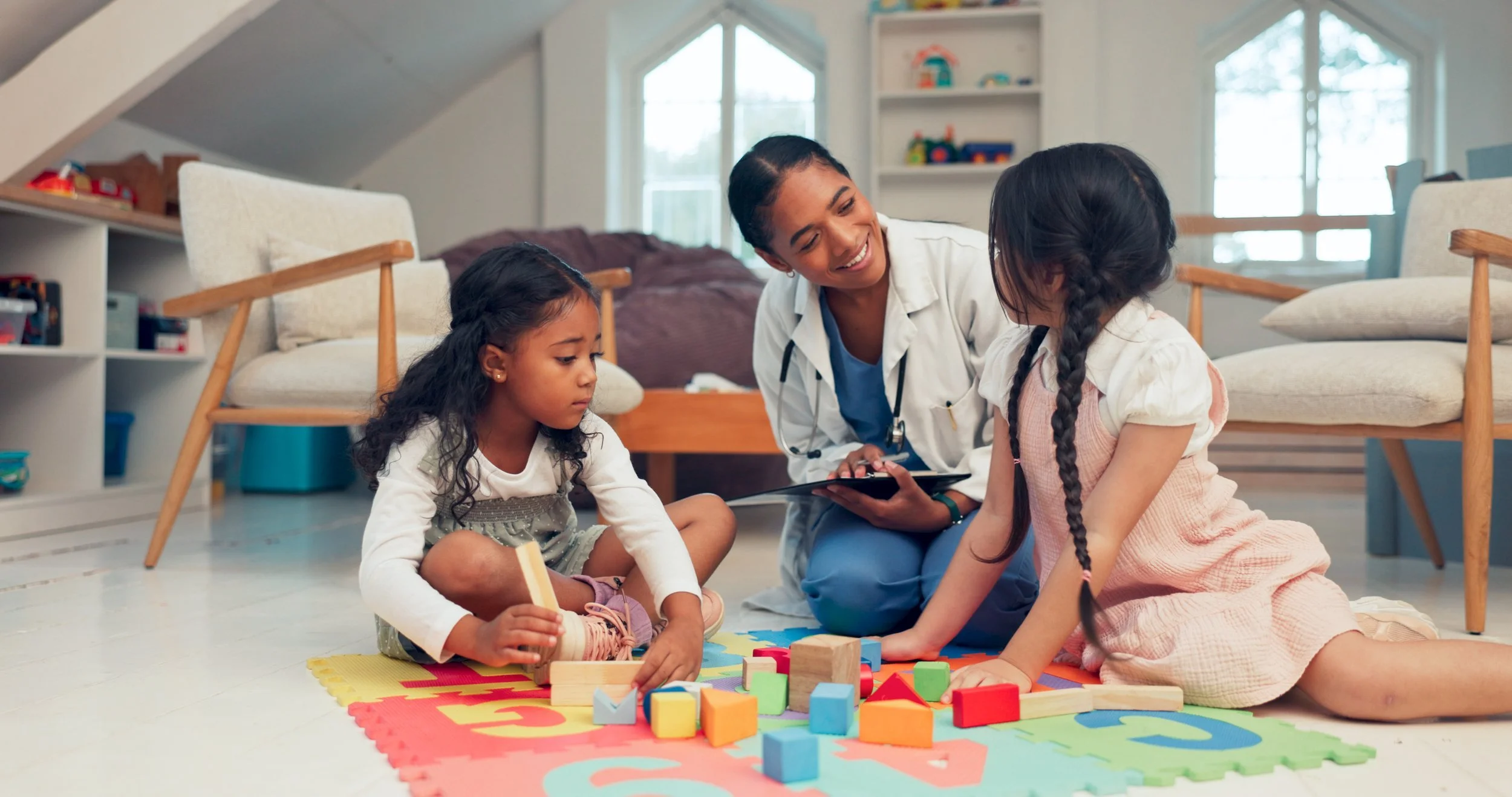a doctor and two children joyfully building structures with colorful blocks on a play mat