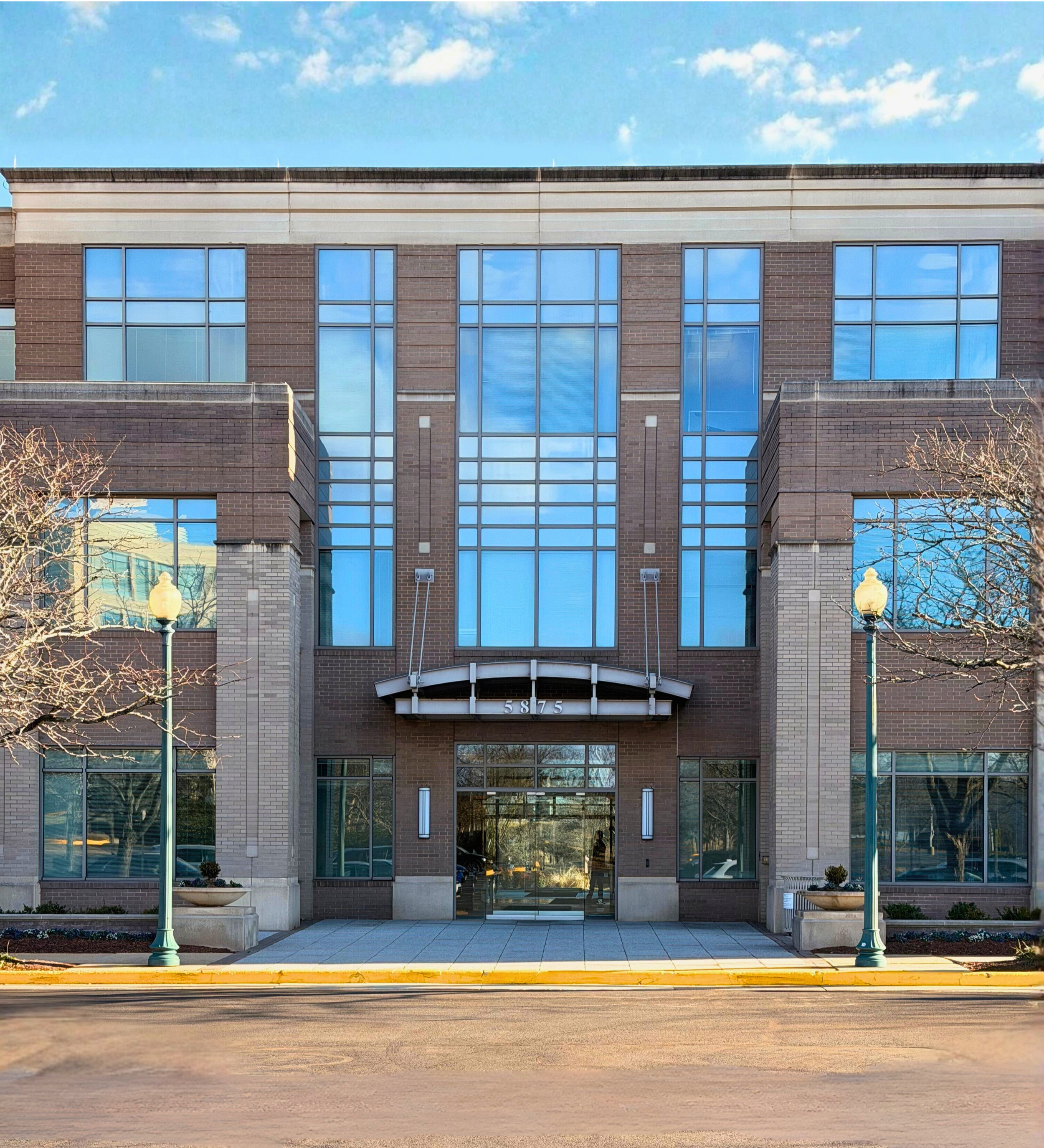 Entrance to a gray brick mid-rise office building with bright blue sunny skies in background and reflected in windows. 