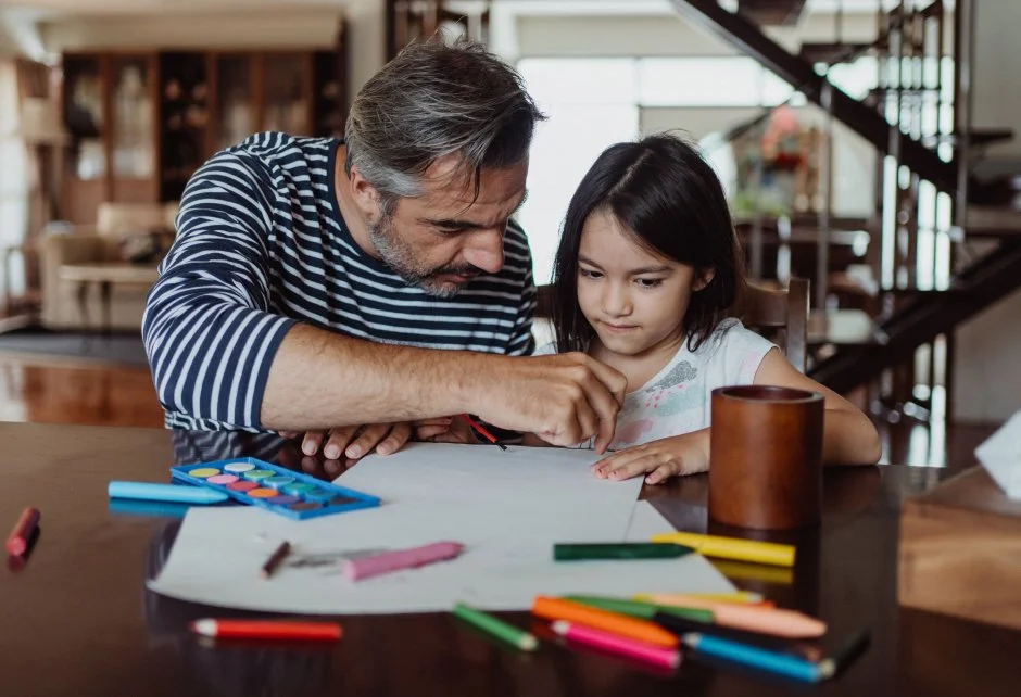 A young girl and her father draw at a table.