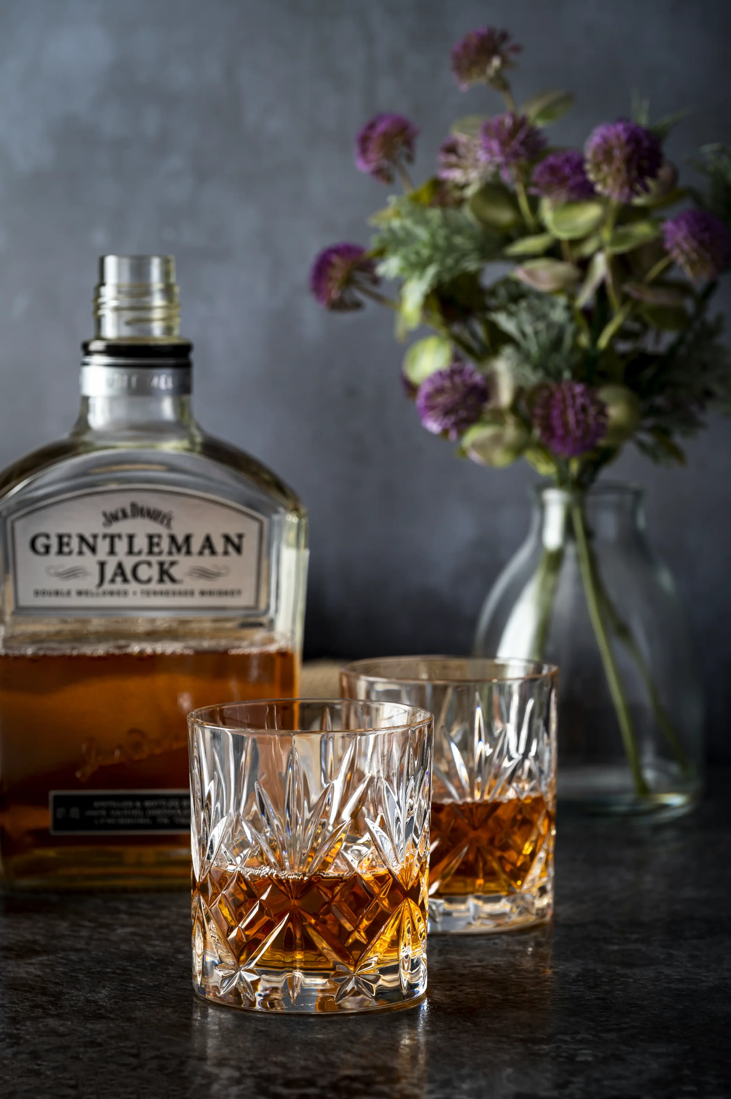 Colour photograph of a bottle of Gentleman Jack Bourbon with two glasses on a dark background
