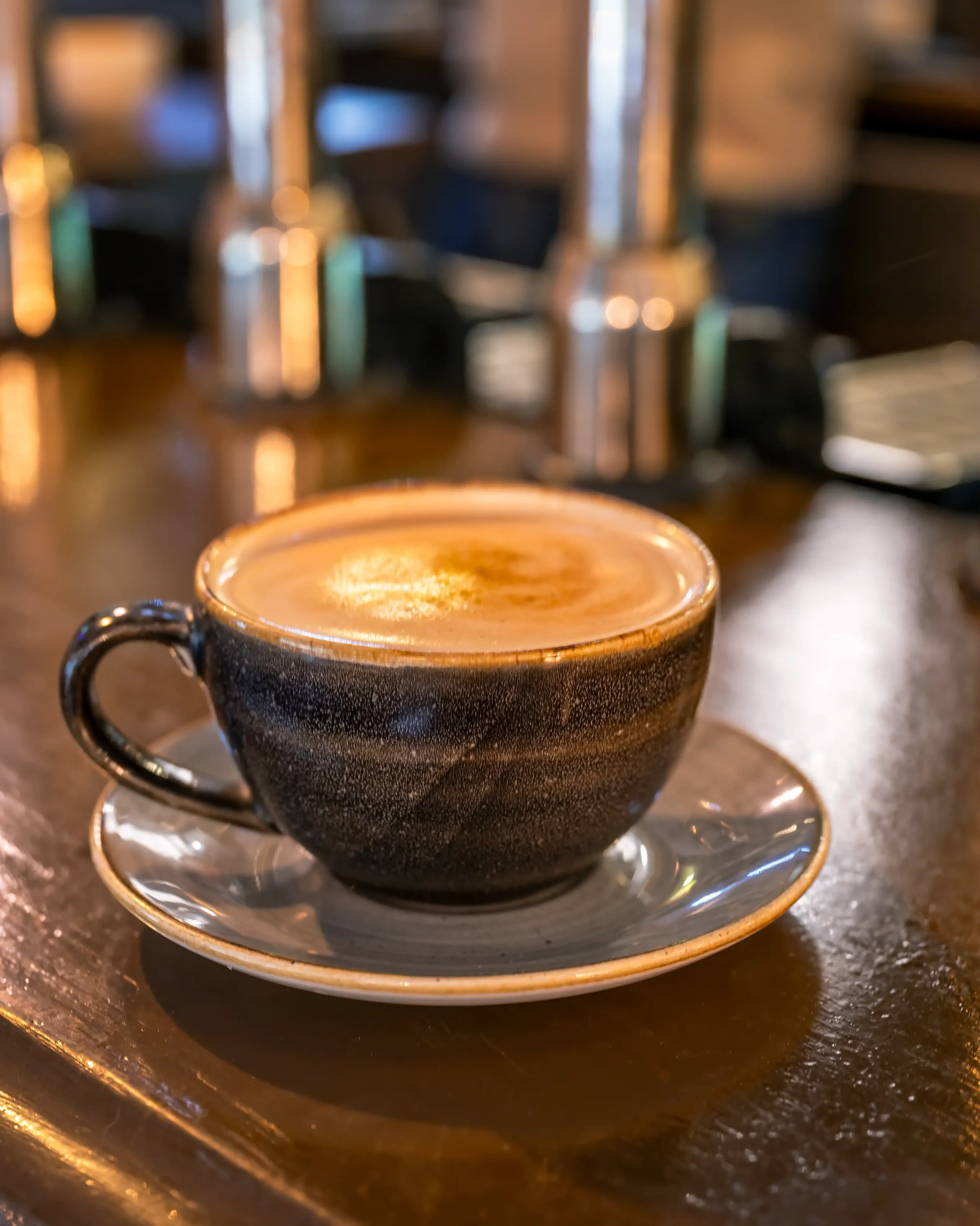 Colour photograph of a cup of coffee in a blue cup sitting on a blue saucer on a bar top