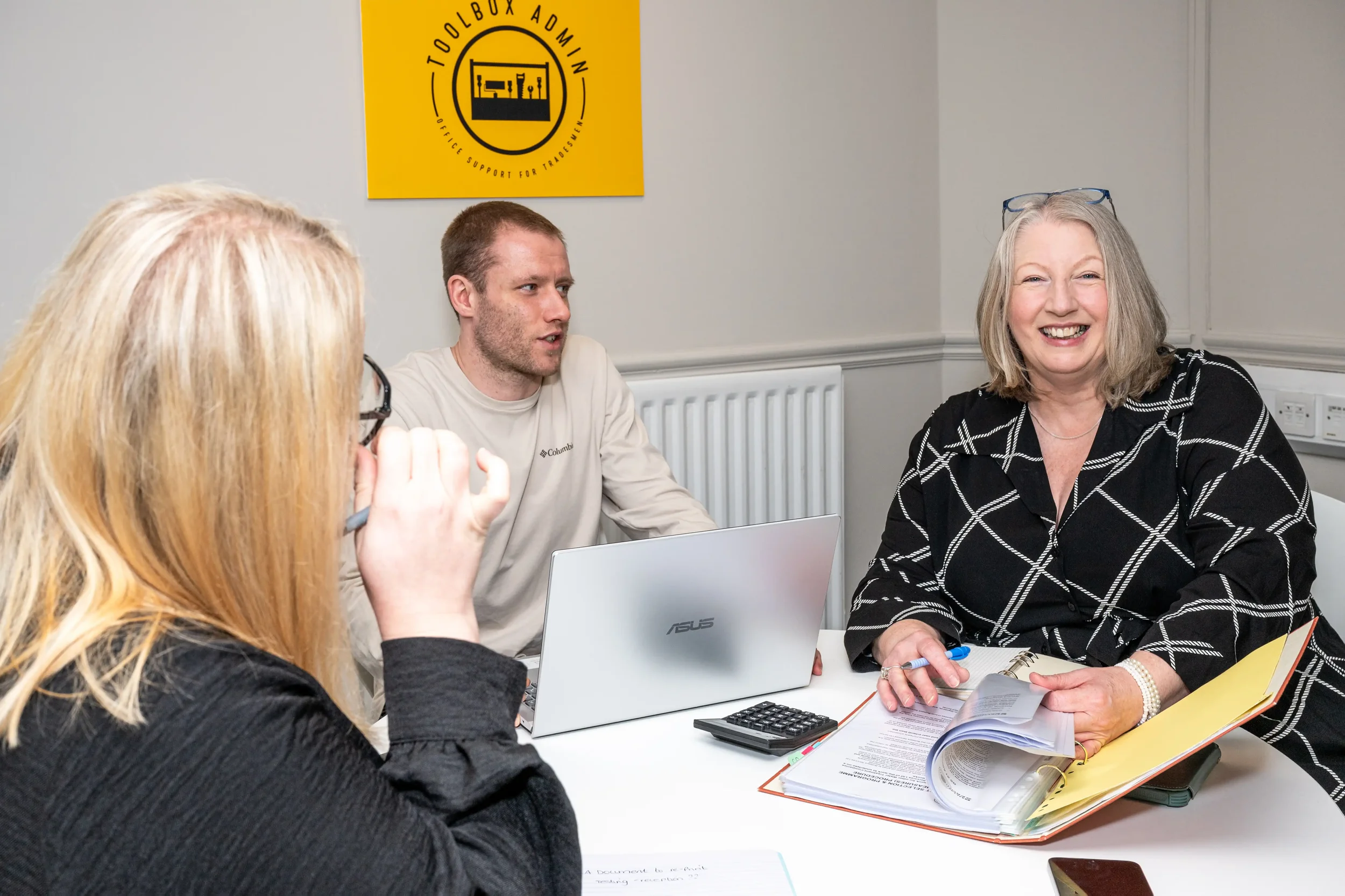Colour photograph of 2 women and a man sitting around a table in a meeting room reviewing client paperwork