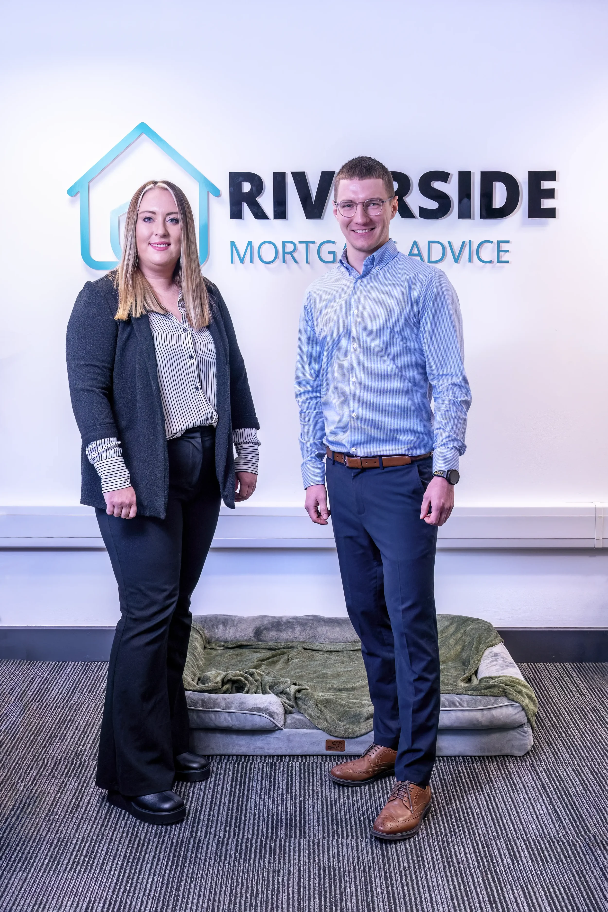 Photograph of a man and a woman standing together in an office, in front of their business sign